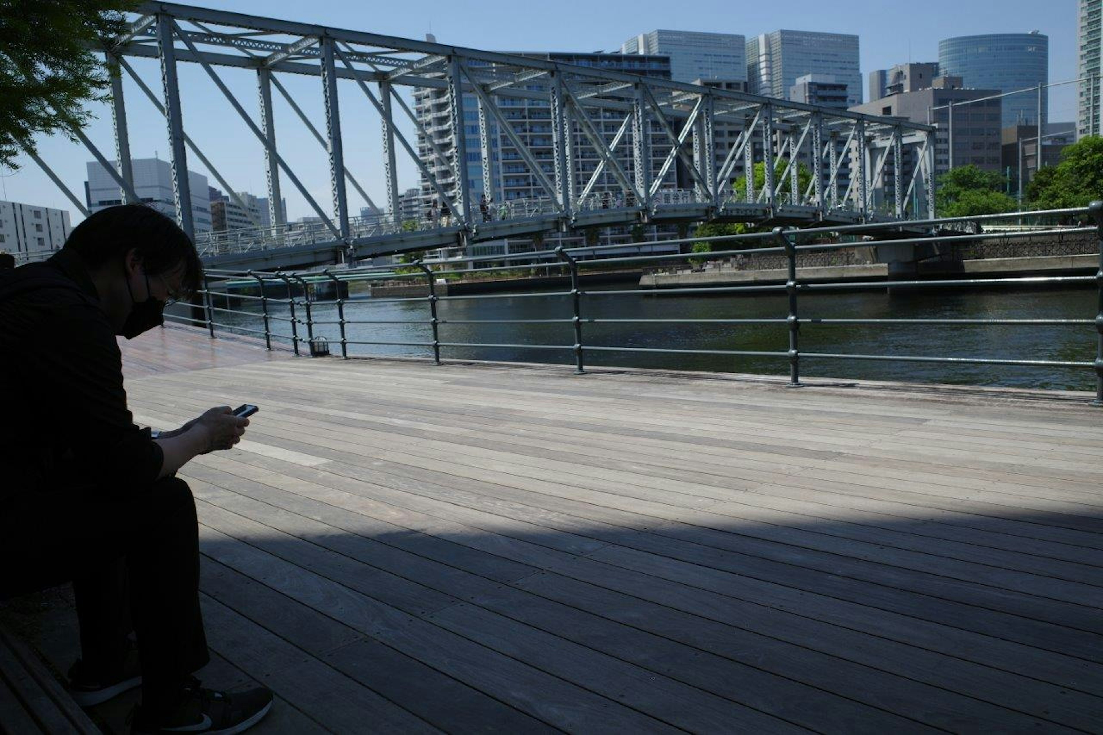 Eine Person sitzt und schaut auf ein Smartphone mit einer Brücke und Gebäuden im Hintergrund