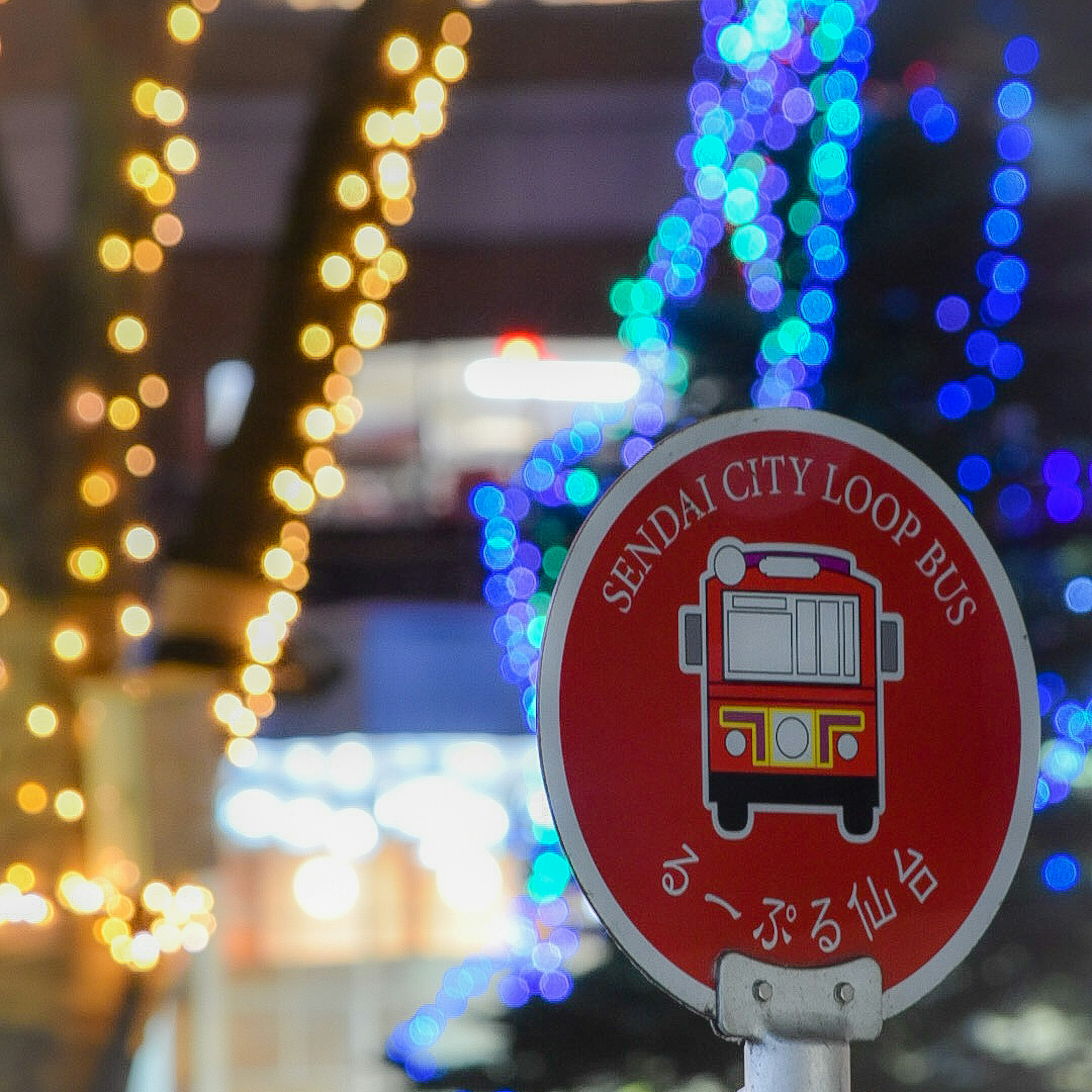 Sendai City Loop Bus sign with colorful lights in the background