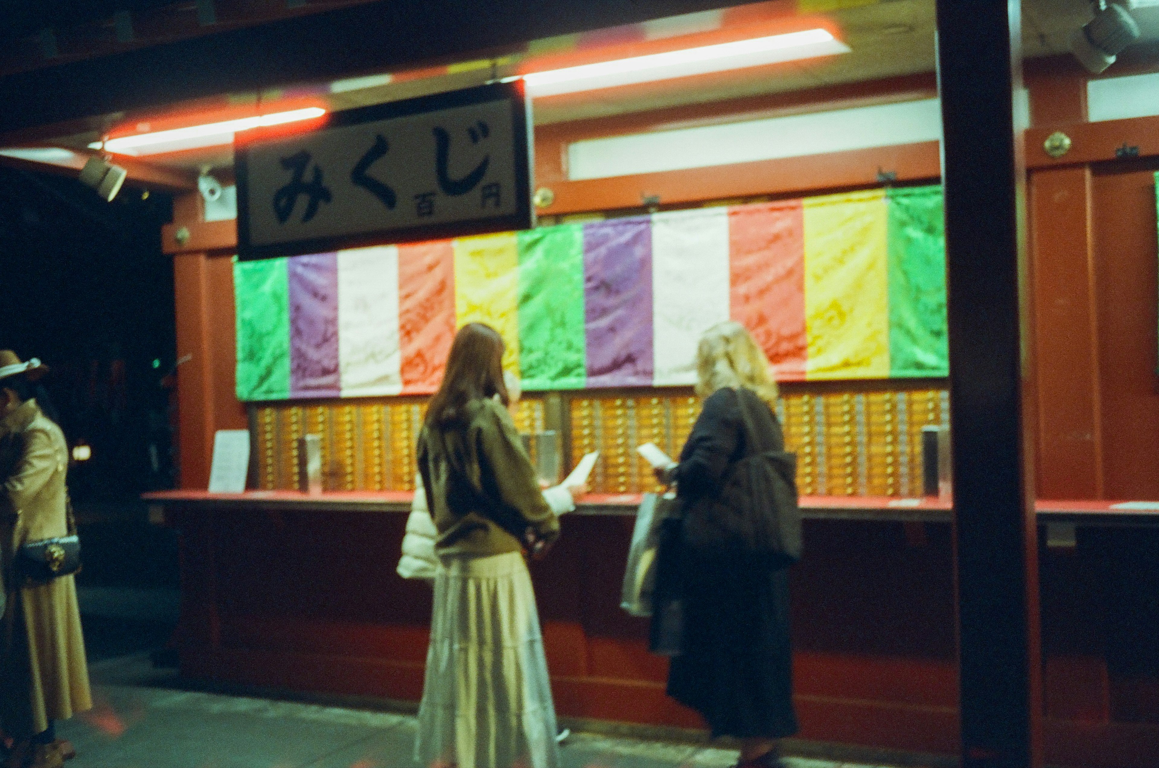 Donne che estraggono omikuji in un santuario di notte Visibili tende colorate e scatole di legno