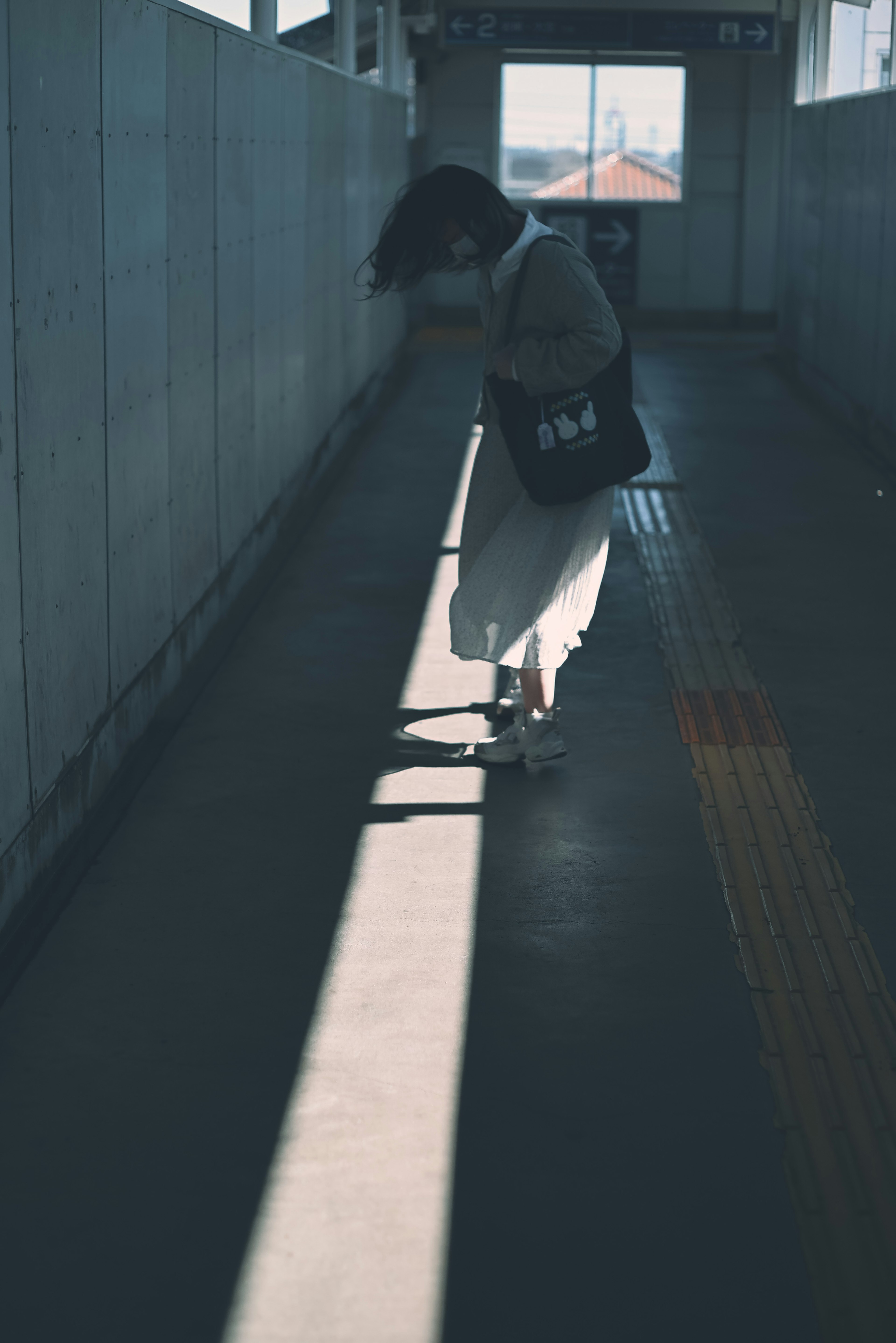 A woman standing in a corridor with sunlight creating shadows