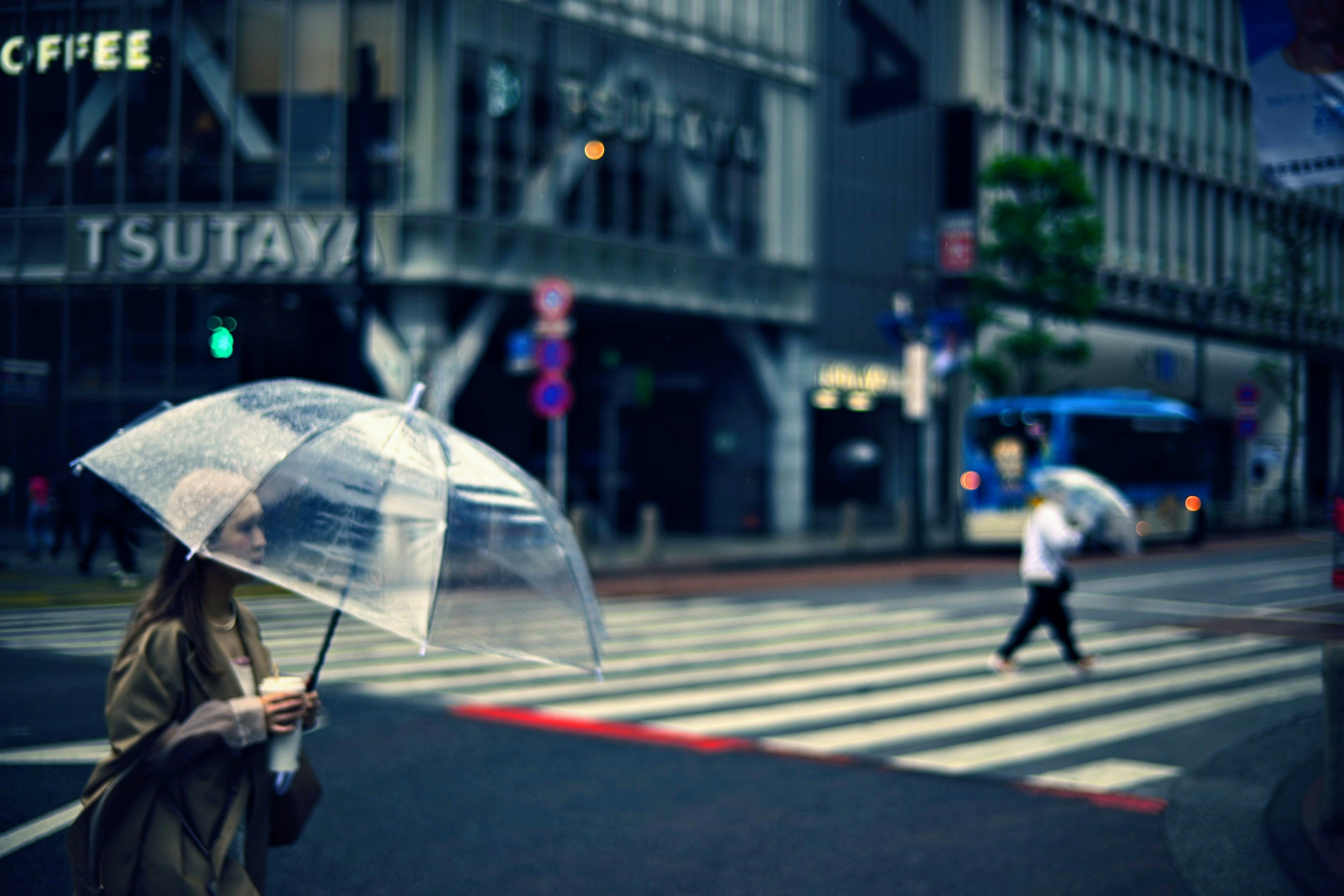 透明な傘を持っている女性が交差点を渡っている街の風景