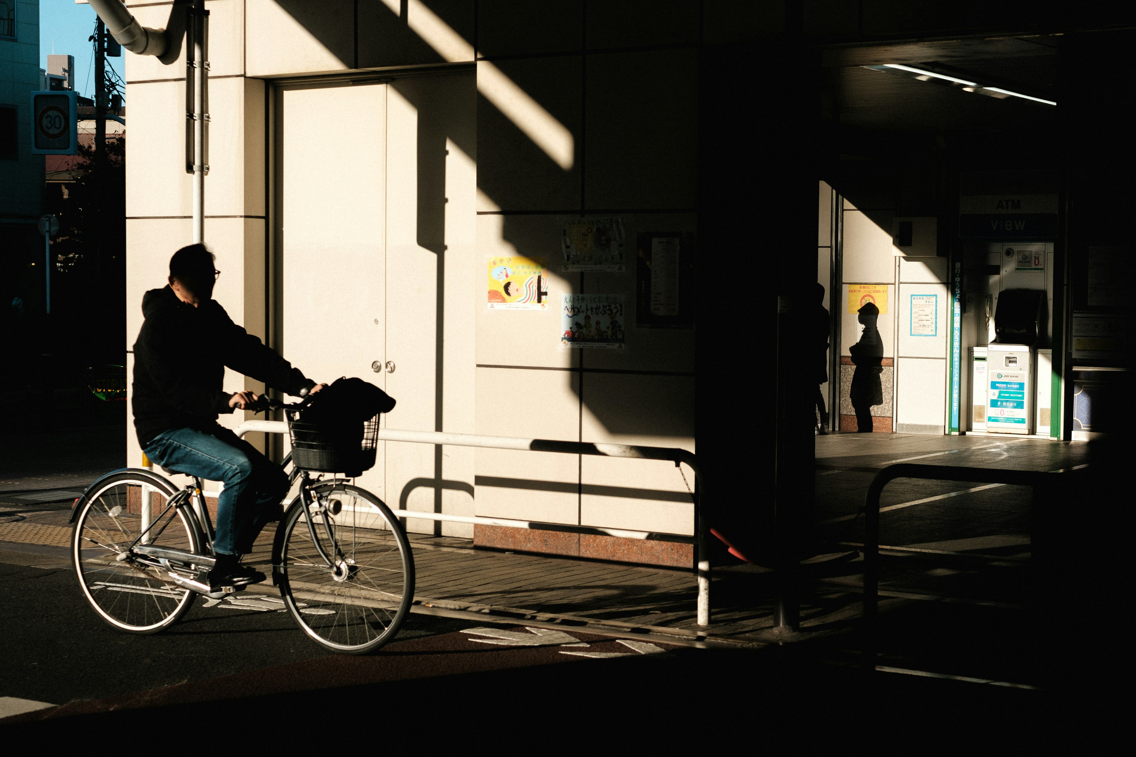 A person riding a bicycle in shadow with a train station entrance in the background