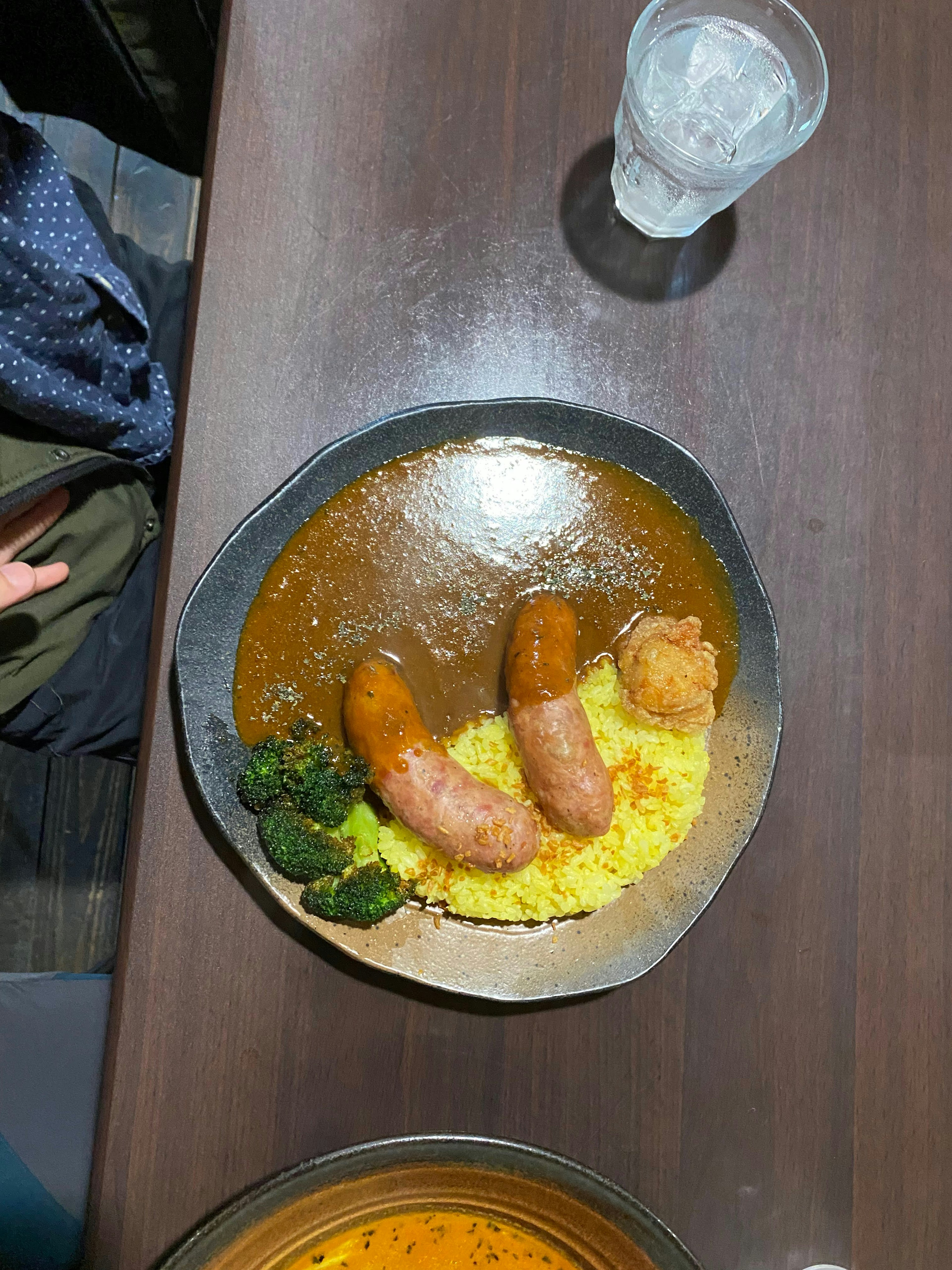 A plate of curry with sausages served alongside broccoli and rice