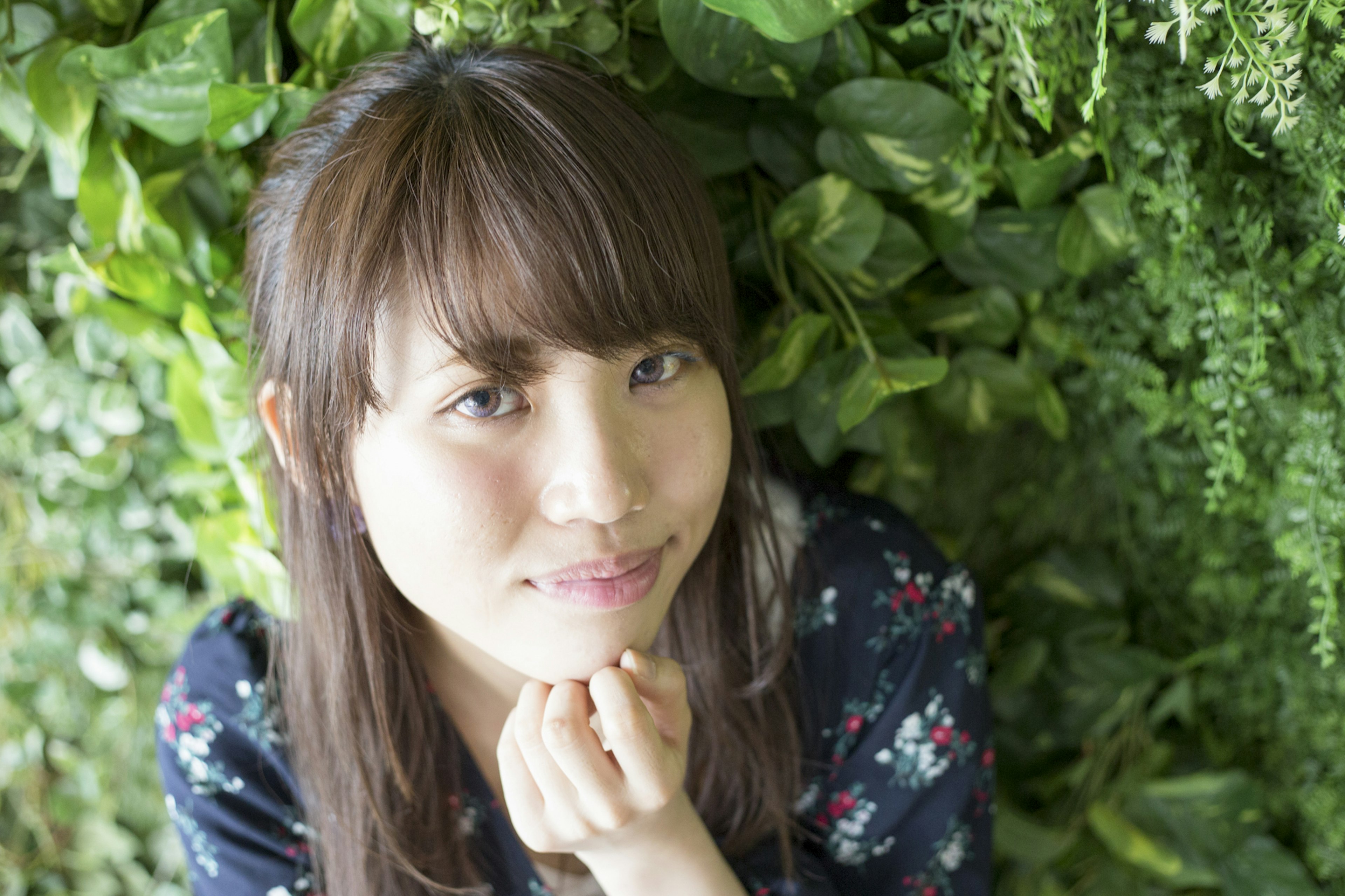 Retrato de una joven frente a una pared de plantas verdes