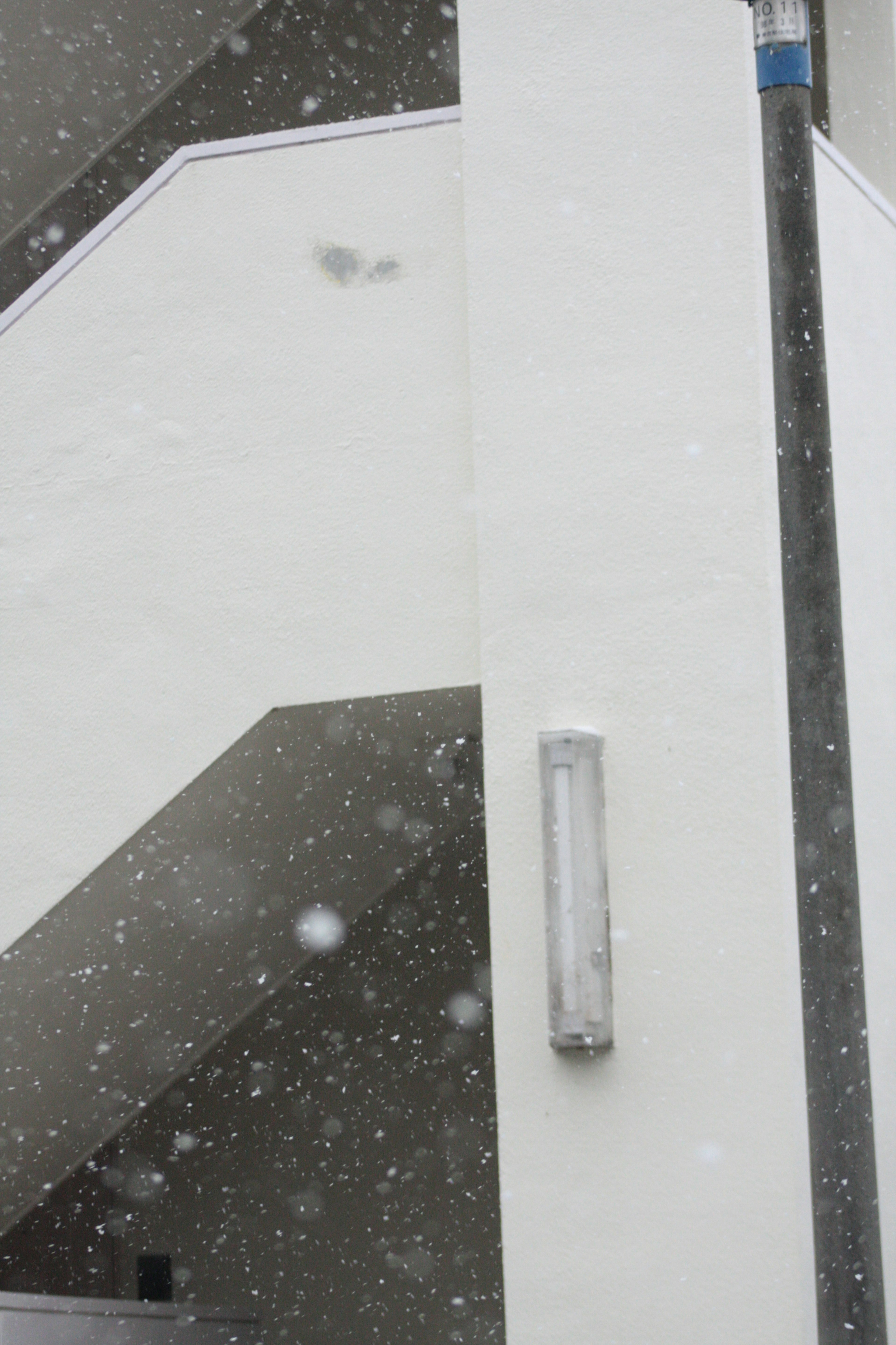 Snow falling against a white wall and staircase