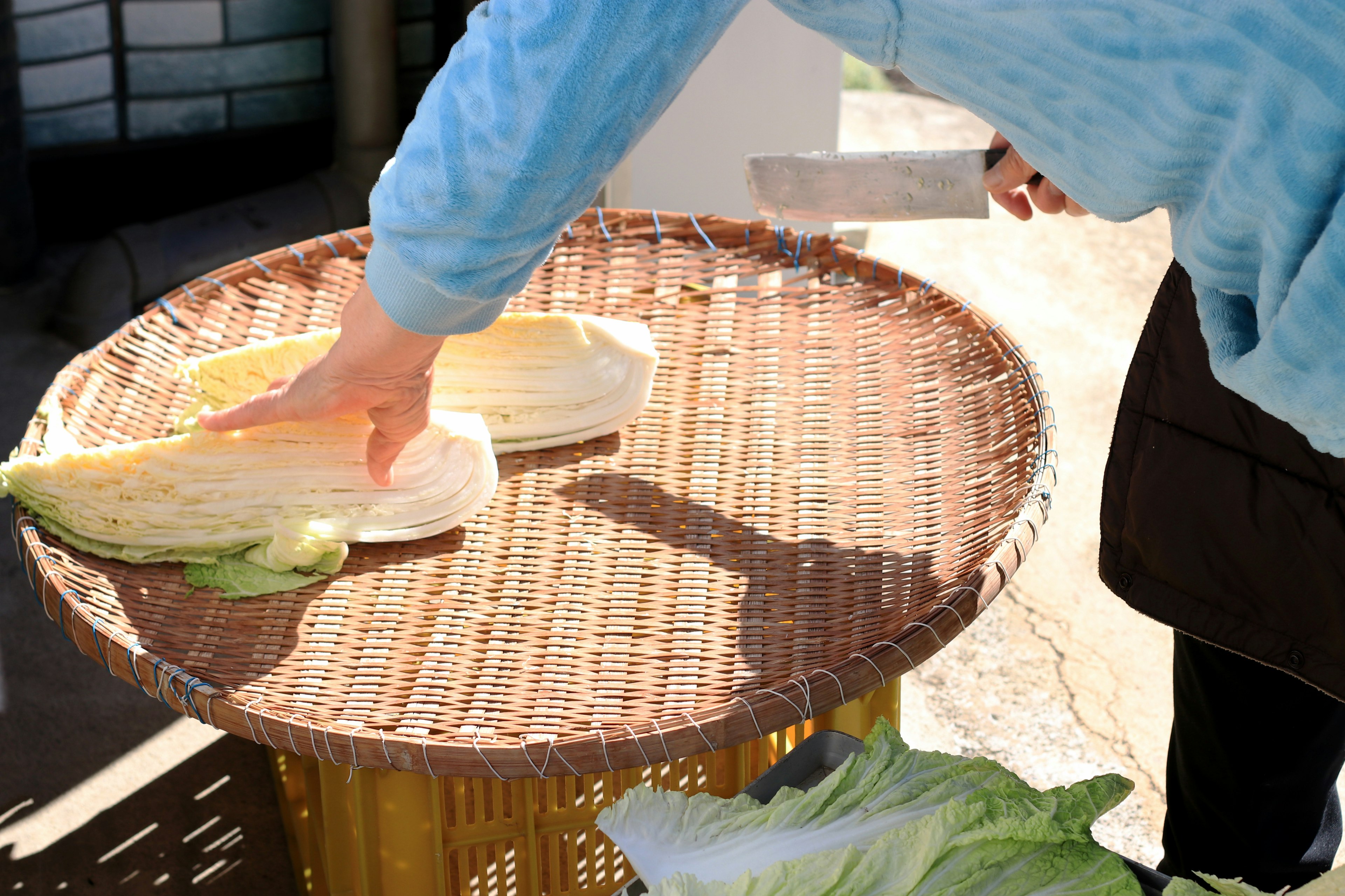 Person in blue shirt cutting cabbage on a wicker table