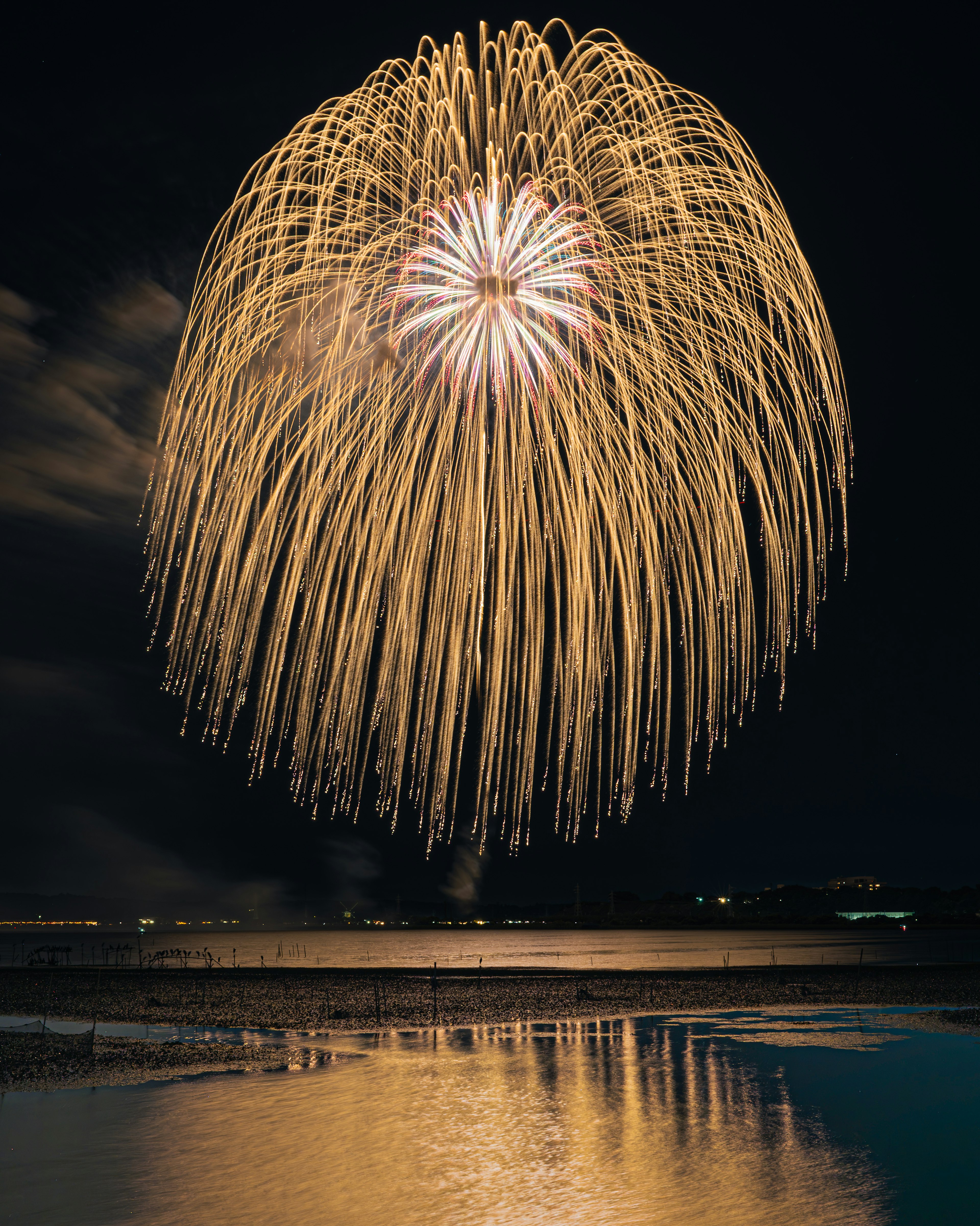 Bellissimo spettacolo di fuochi d'artificio dorati che esplodono nel cielo notturno riflettendosi sull'acqua