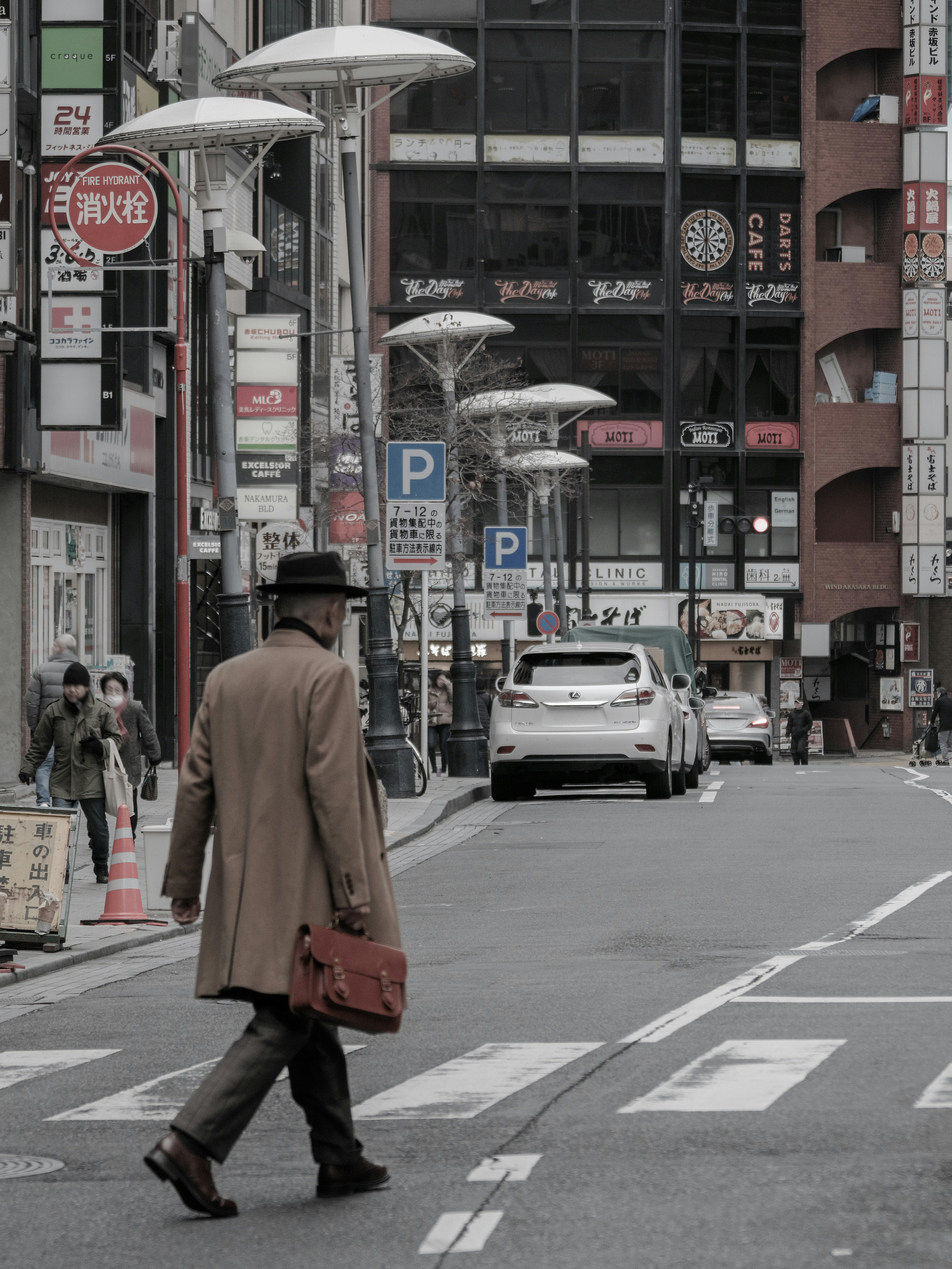 Un hombre caminando por la calle con un abrigo marrón y un sombrero edificios y señales de estacionamiento visibles