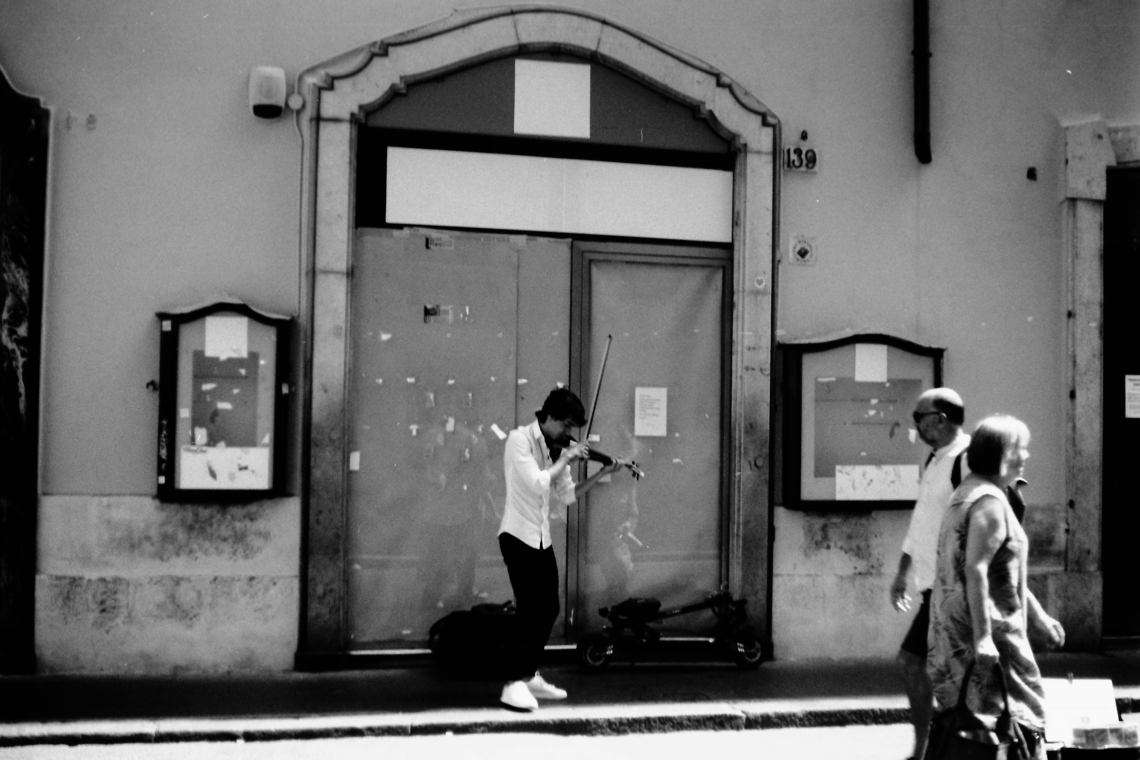 Black and white street scene featuring a violinist performing and pedestrians walking