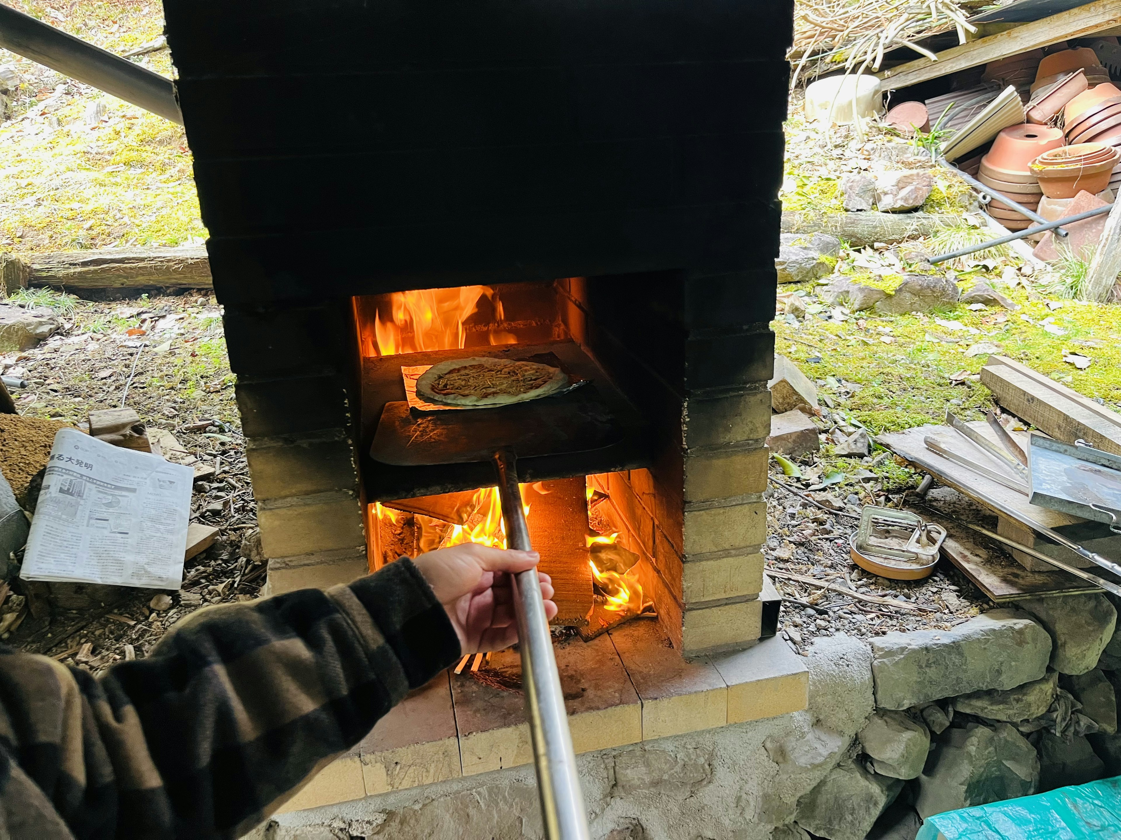 Hand inserting a pizza into a wood-fired oven