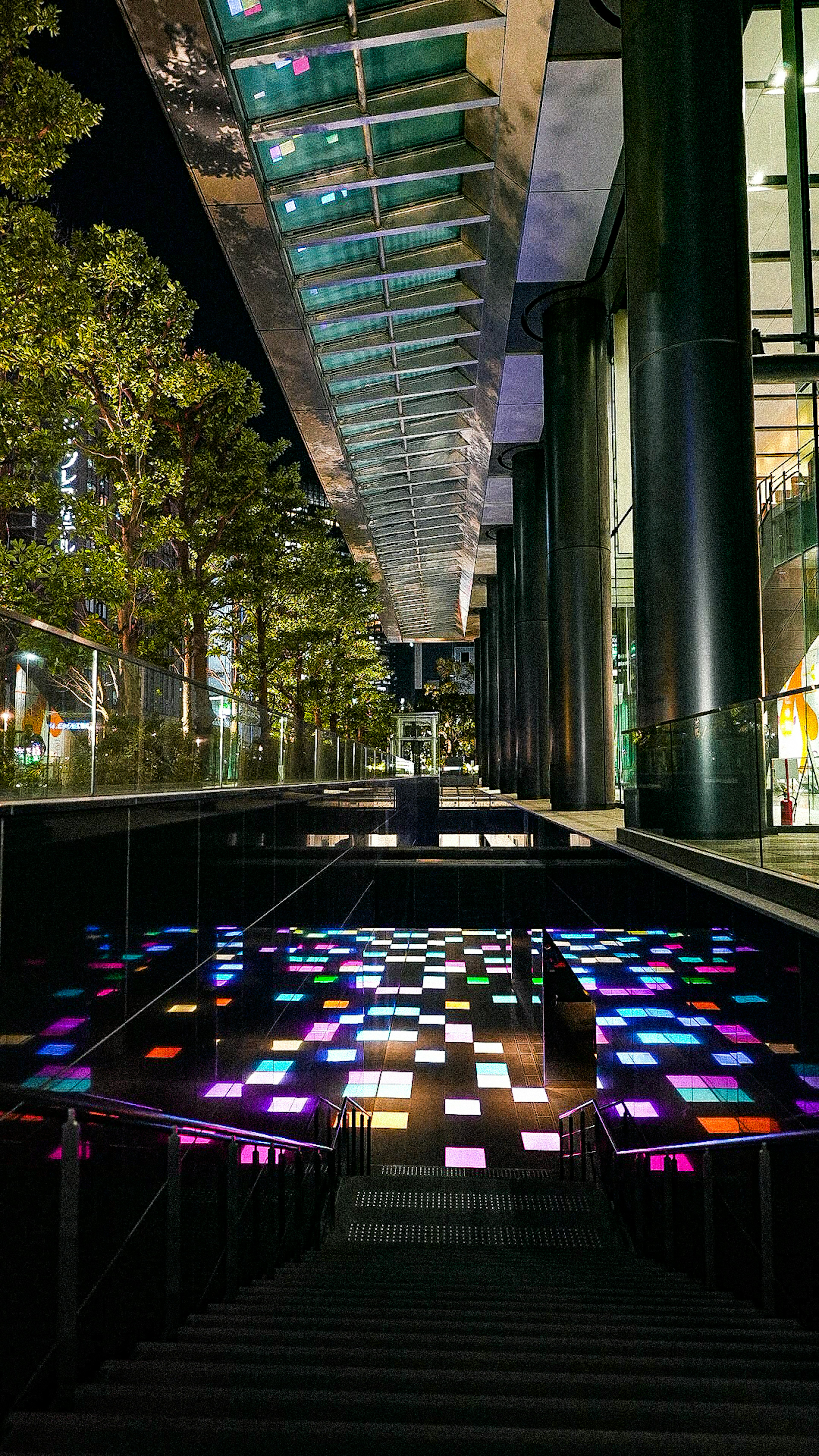 Scène urbaine nocturne avec des panneaux lumineux colorés le long d'un escalier