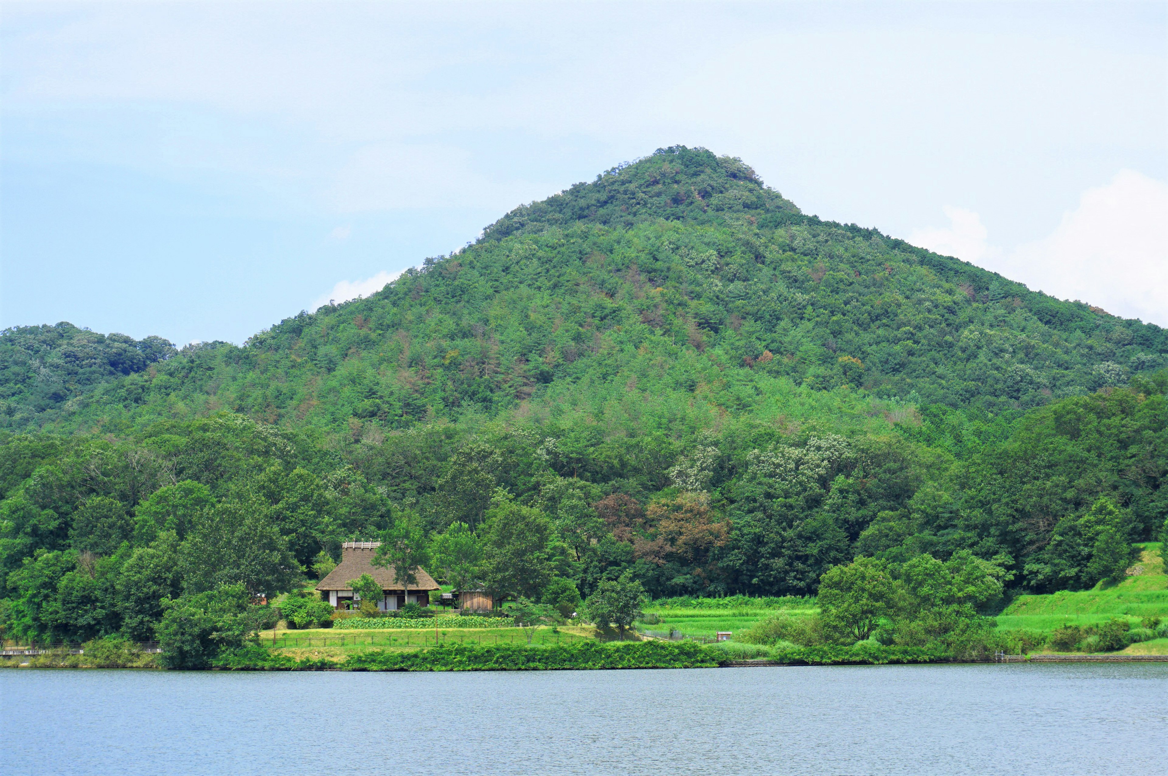 Pemandangan indah gunung hijau dan rumah kecil di dekat danau tenang