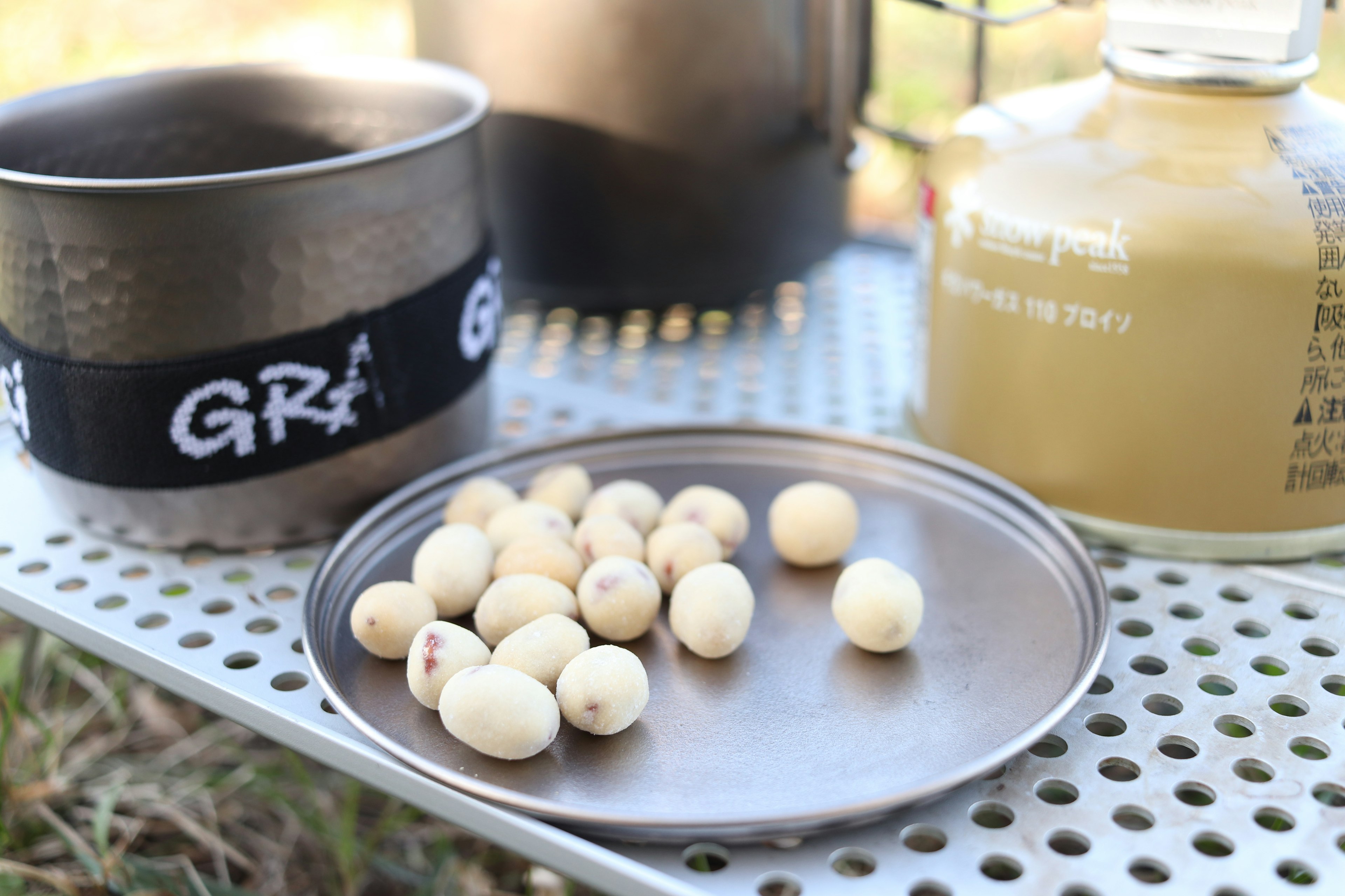 Outdoor scene featuring white beans on a metal plate with a golden container