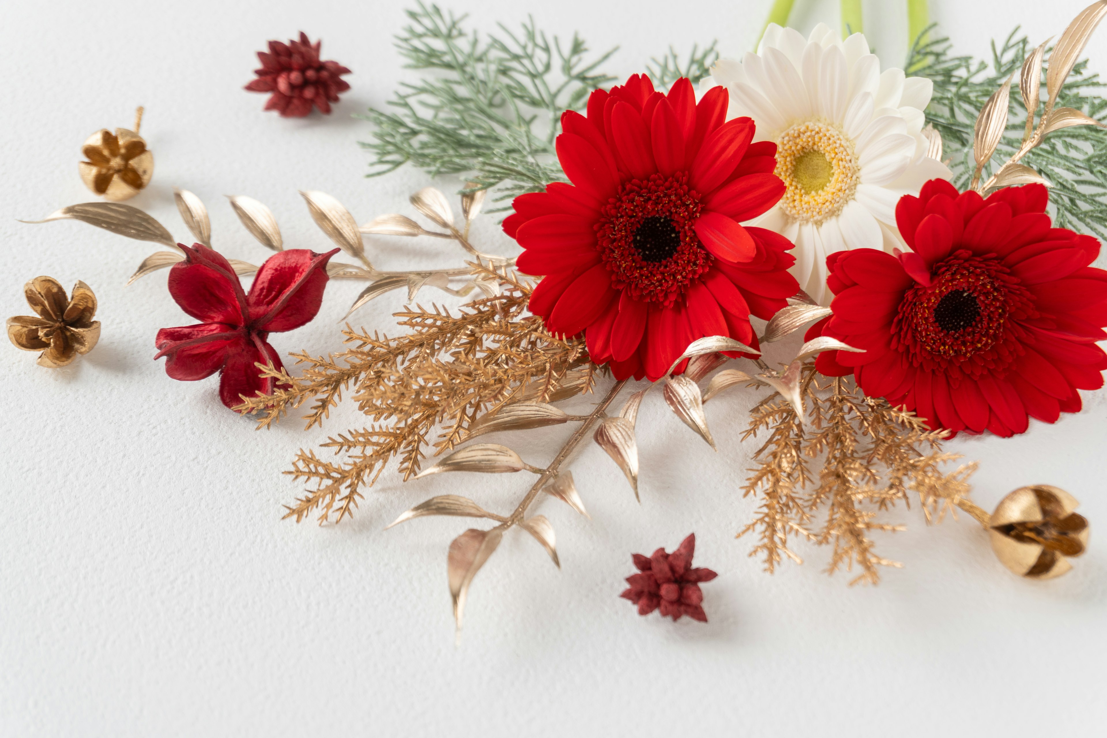 Arrangement of red gerbera and white flower with gold leaves and red decorative flowers