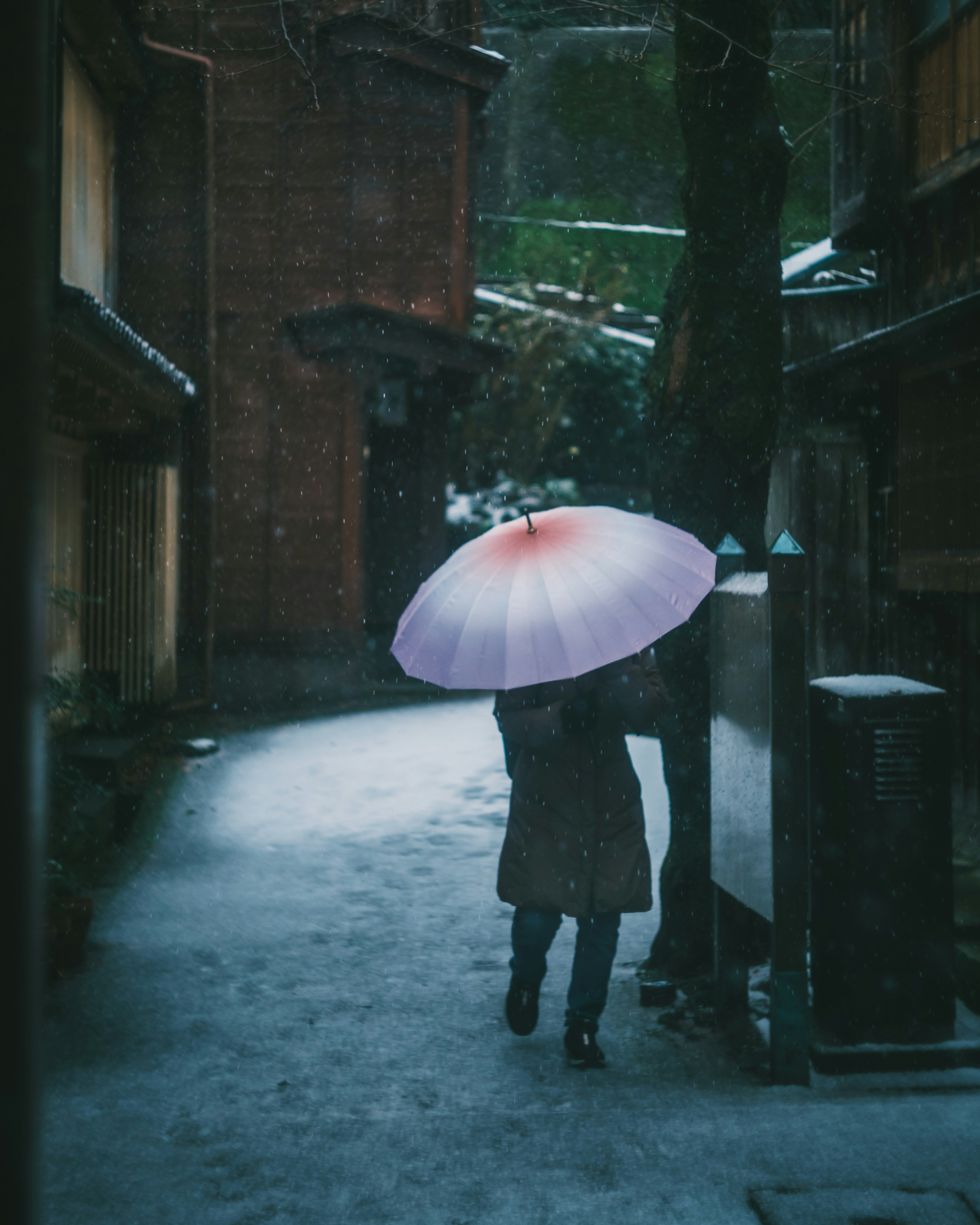 Person walking in the snow holding a colorful umbrella in an old street scene