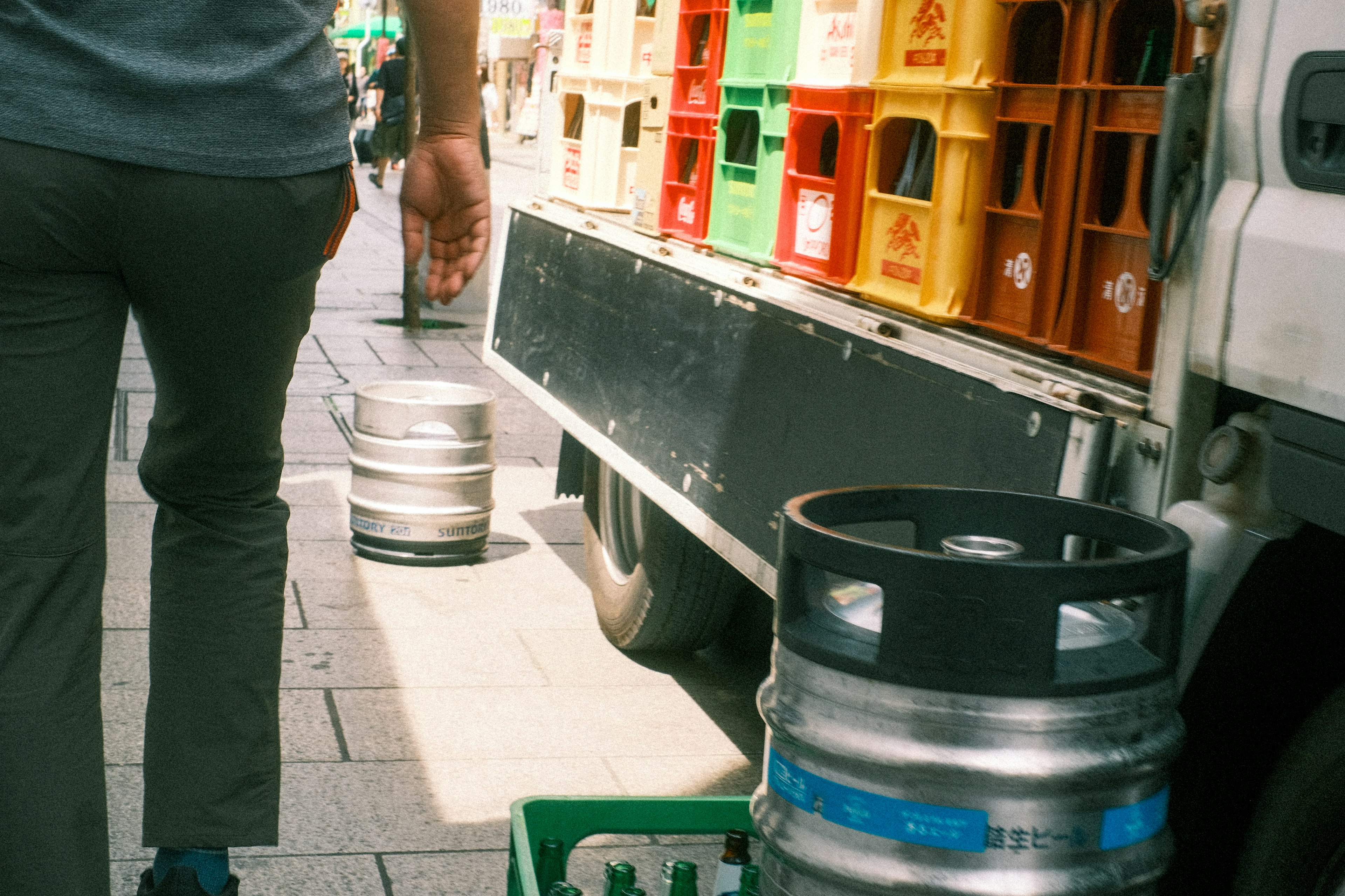 Persona llevando un barril de cerveza junto a un camión con cajas de cerveza de colores