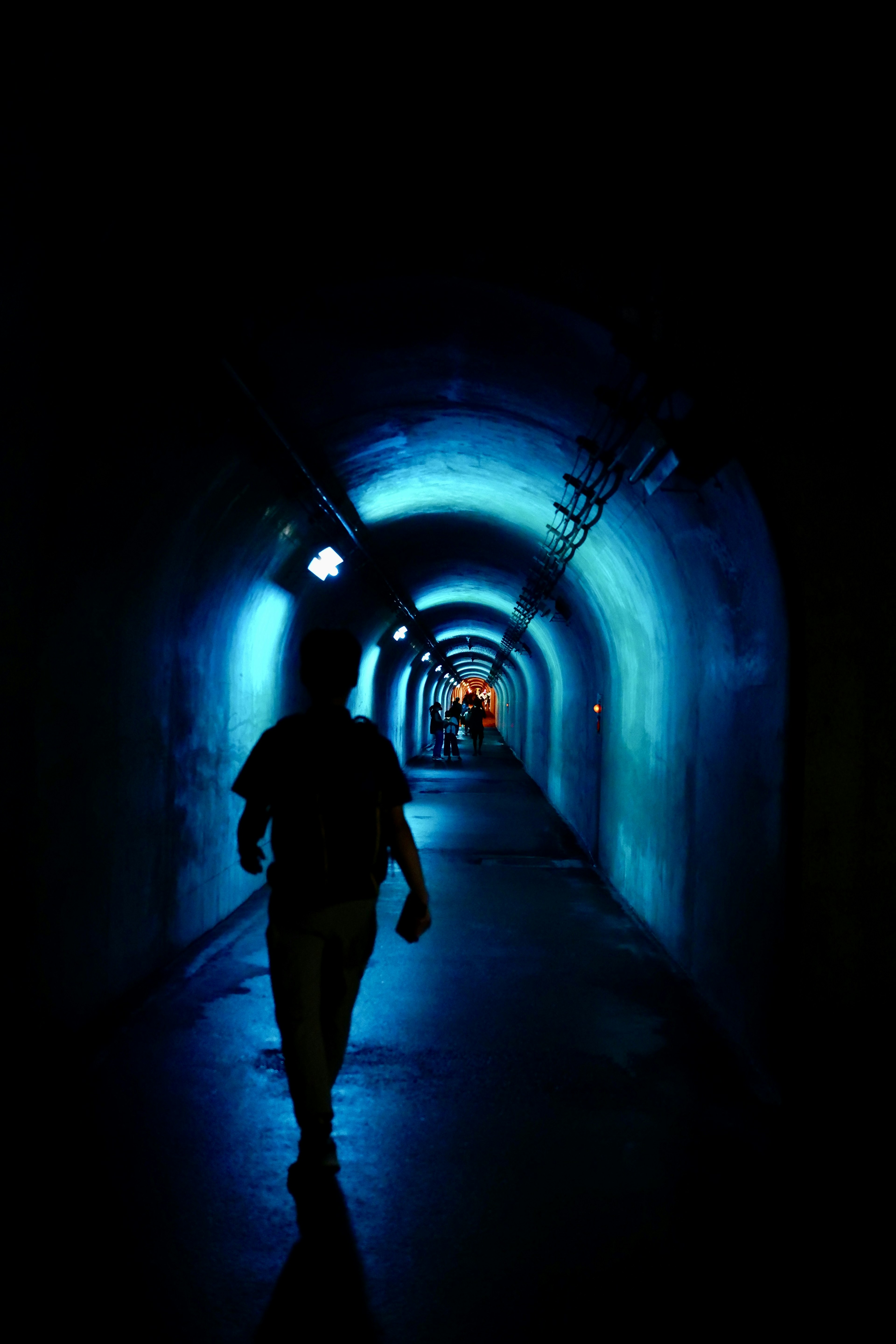 Silhouette di una persona che cammina in un tunnel buio illuminato da luci blu