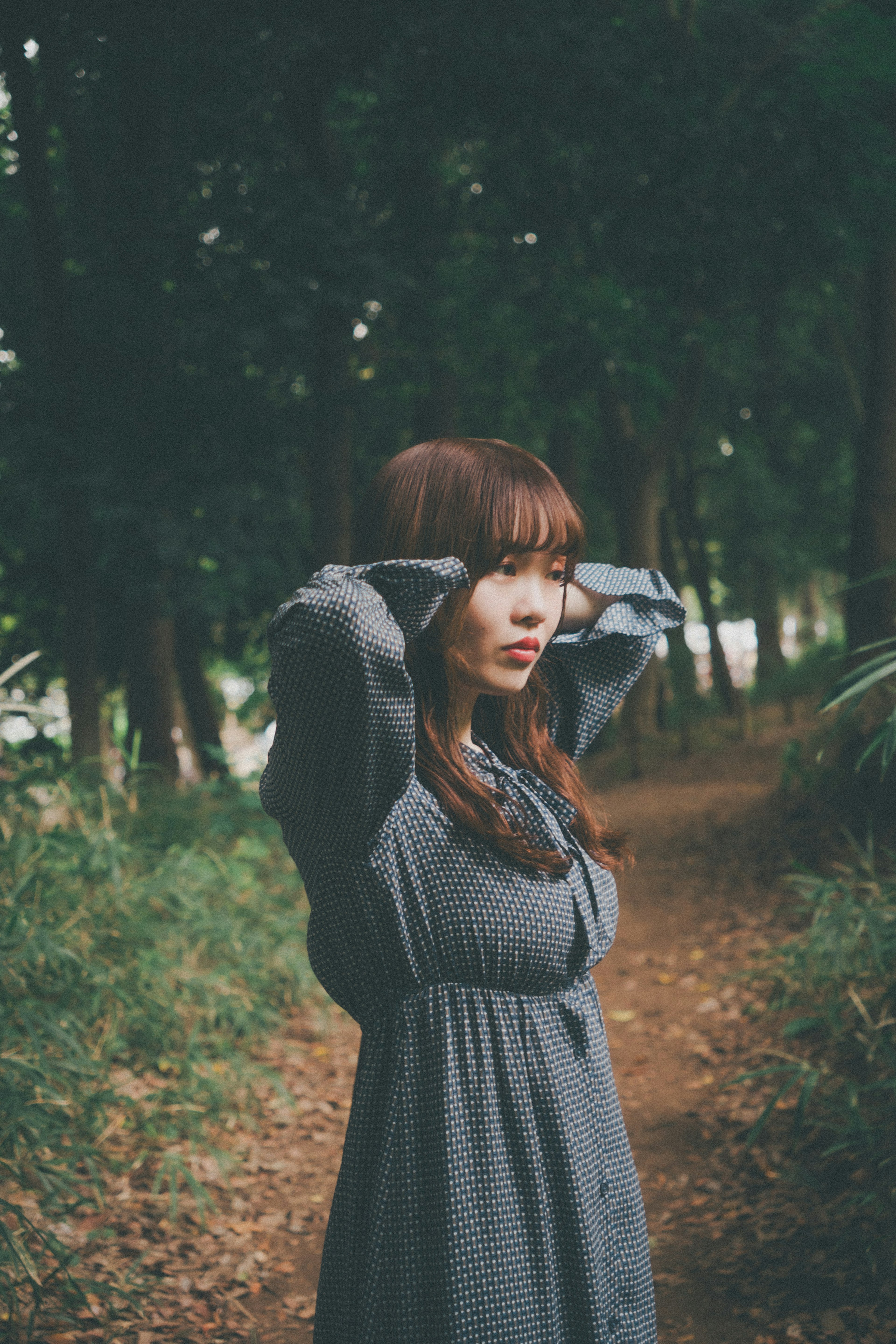 A woman posing in a forest with a green background and a path lined with fallen leaves