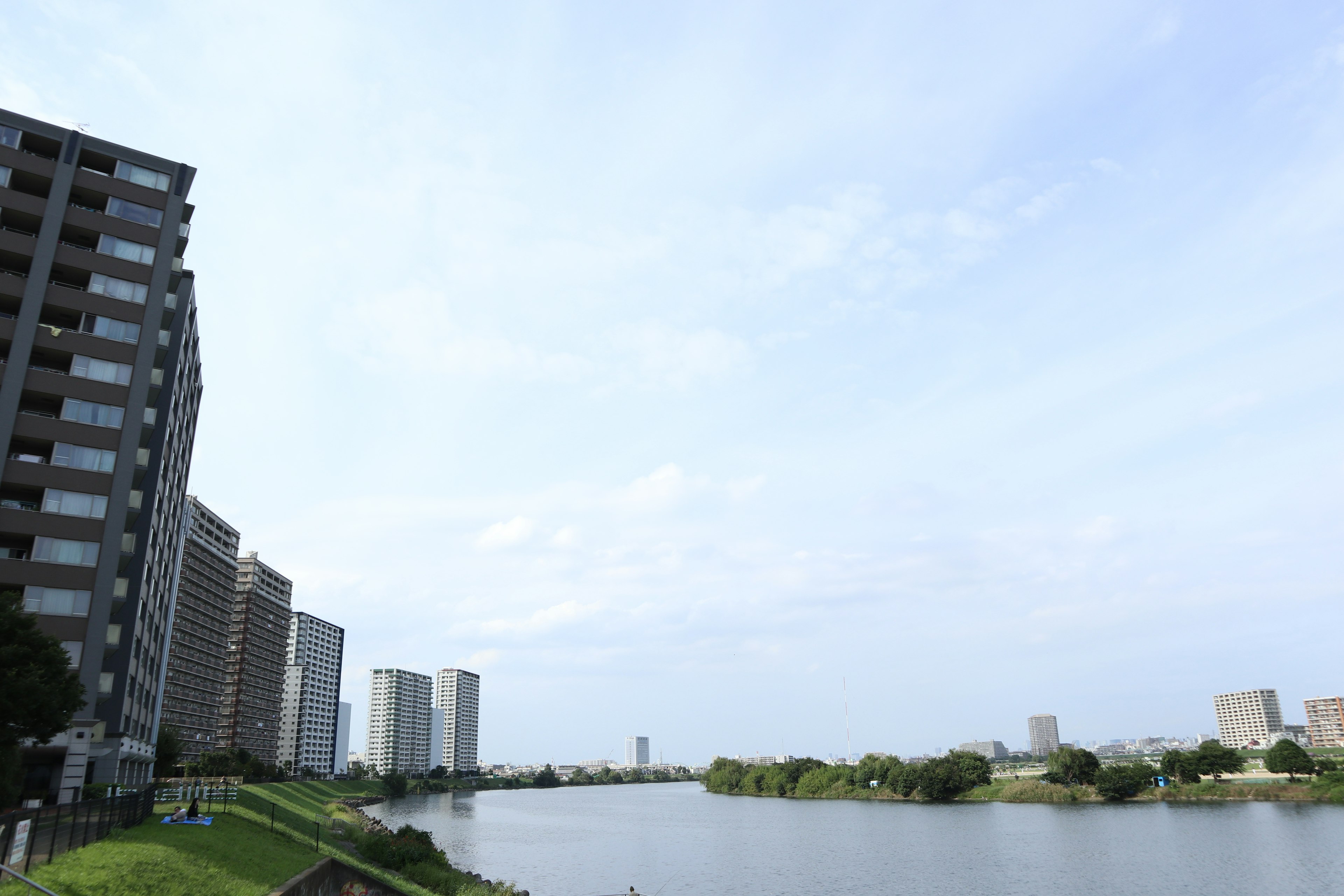 View of residential buildings beside a calm river under a blue sky with green grass