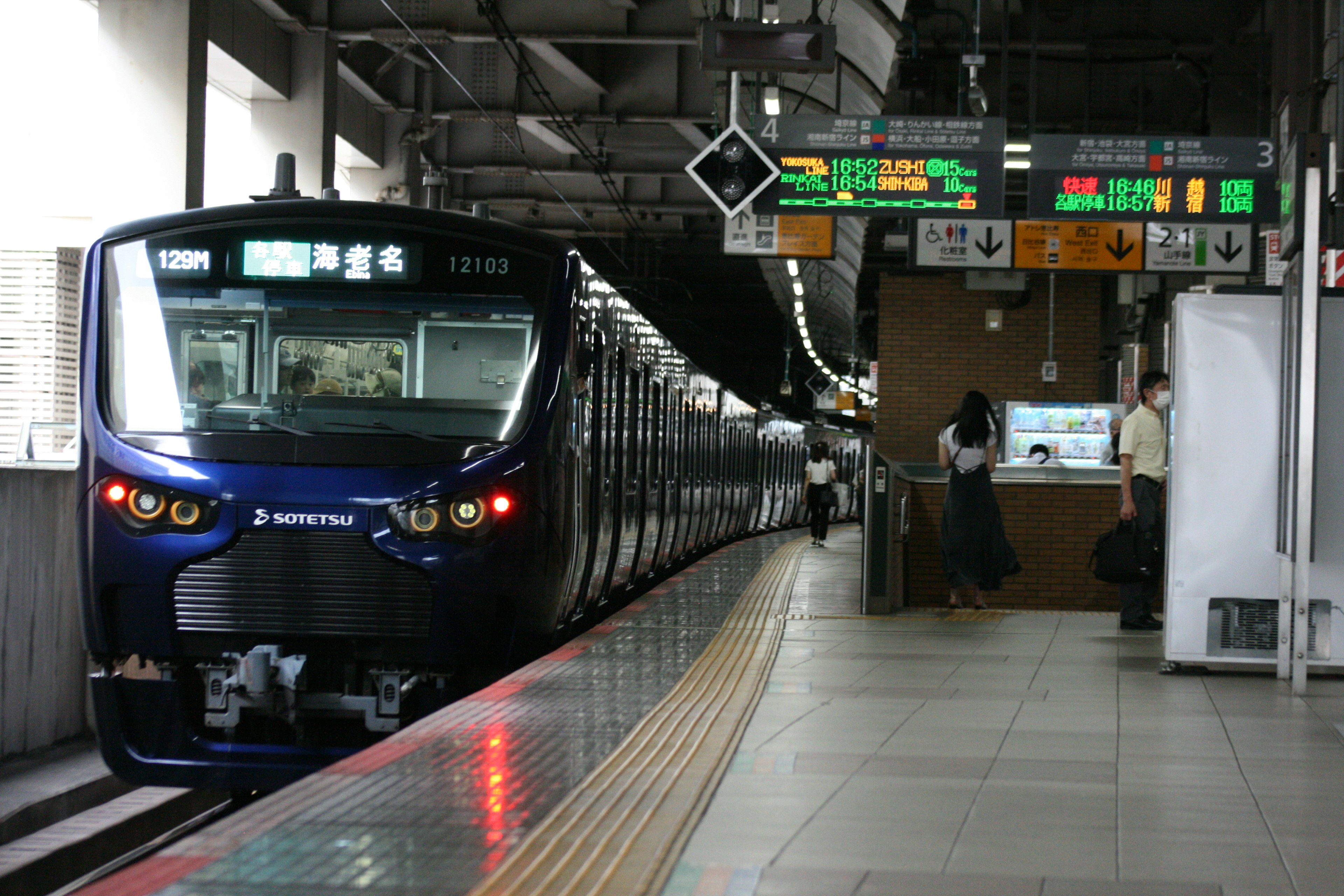 A blue train stopped at a train station with digital displays