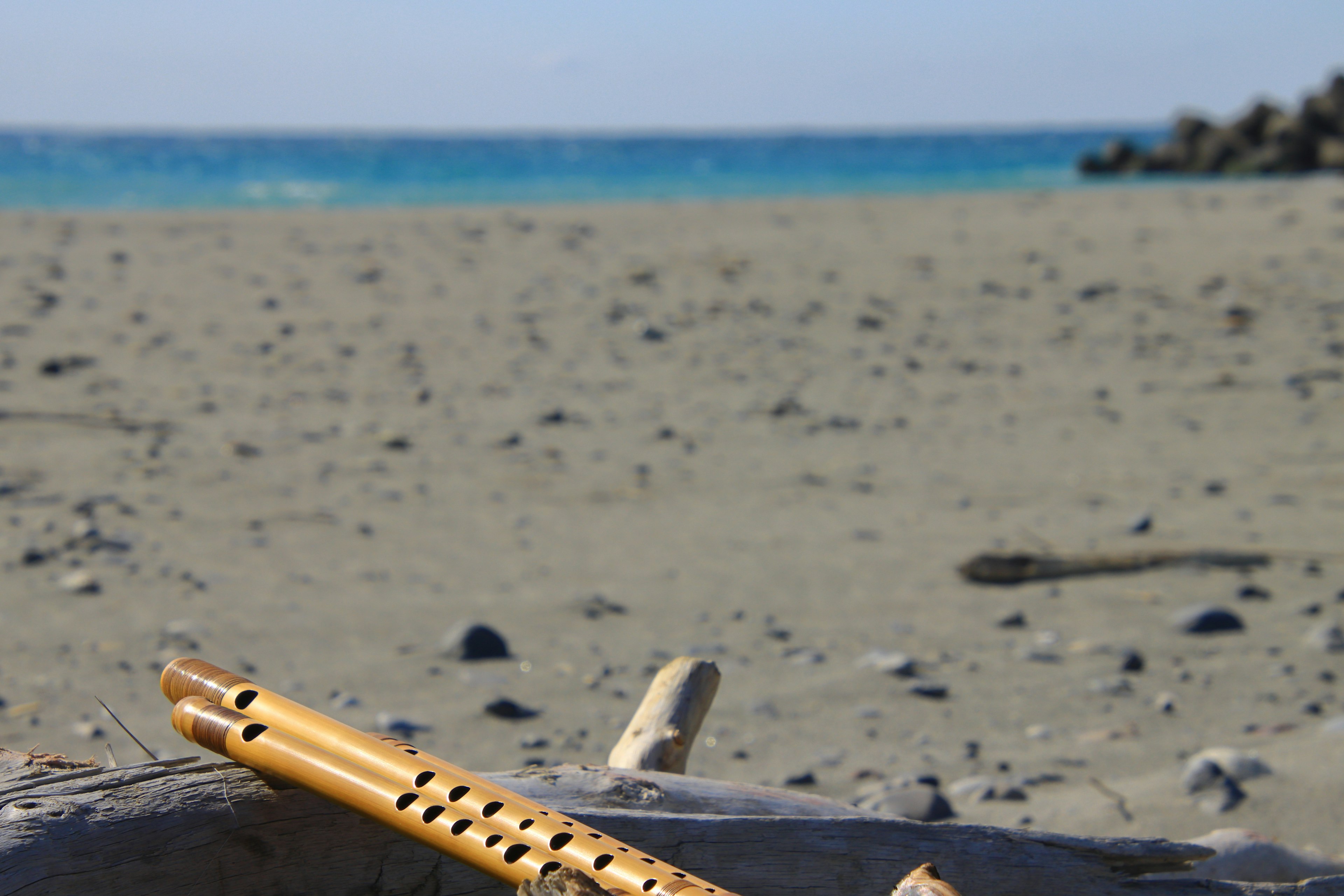 Bamboo flute resting on sandy beach with blue ocean in background