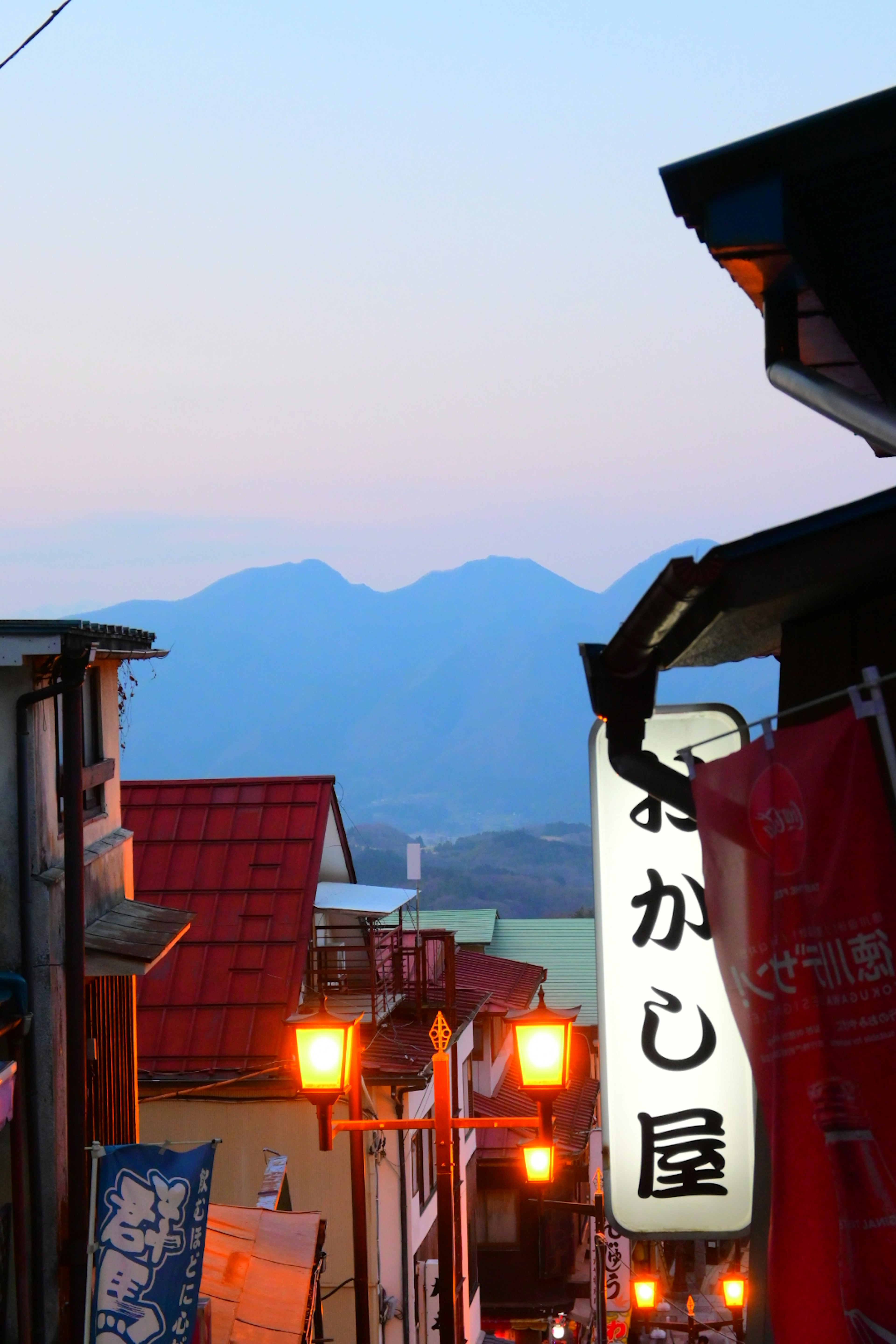 Street view at dusk with mountains in the background featuring lanterns and signs