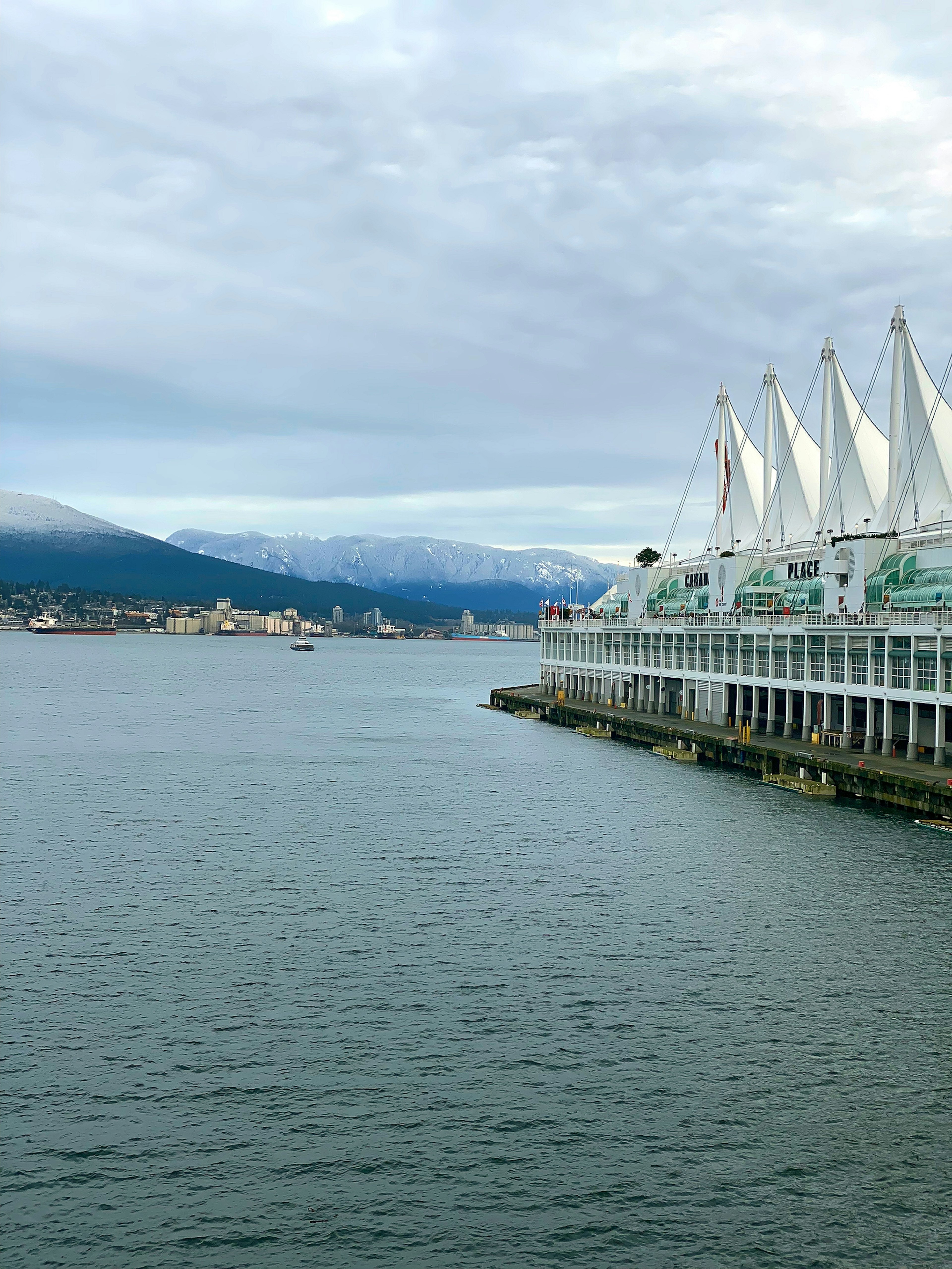 Building with white sails by the water with mountains in the background