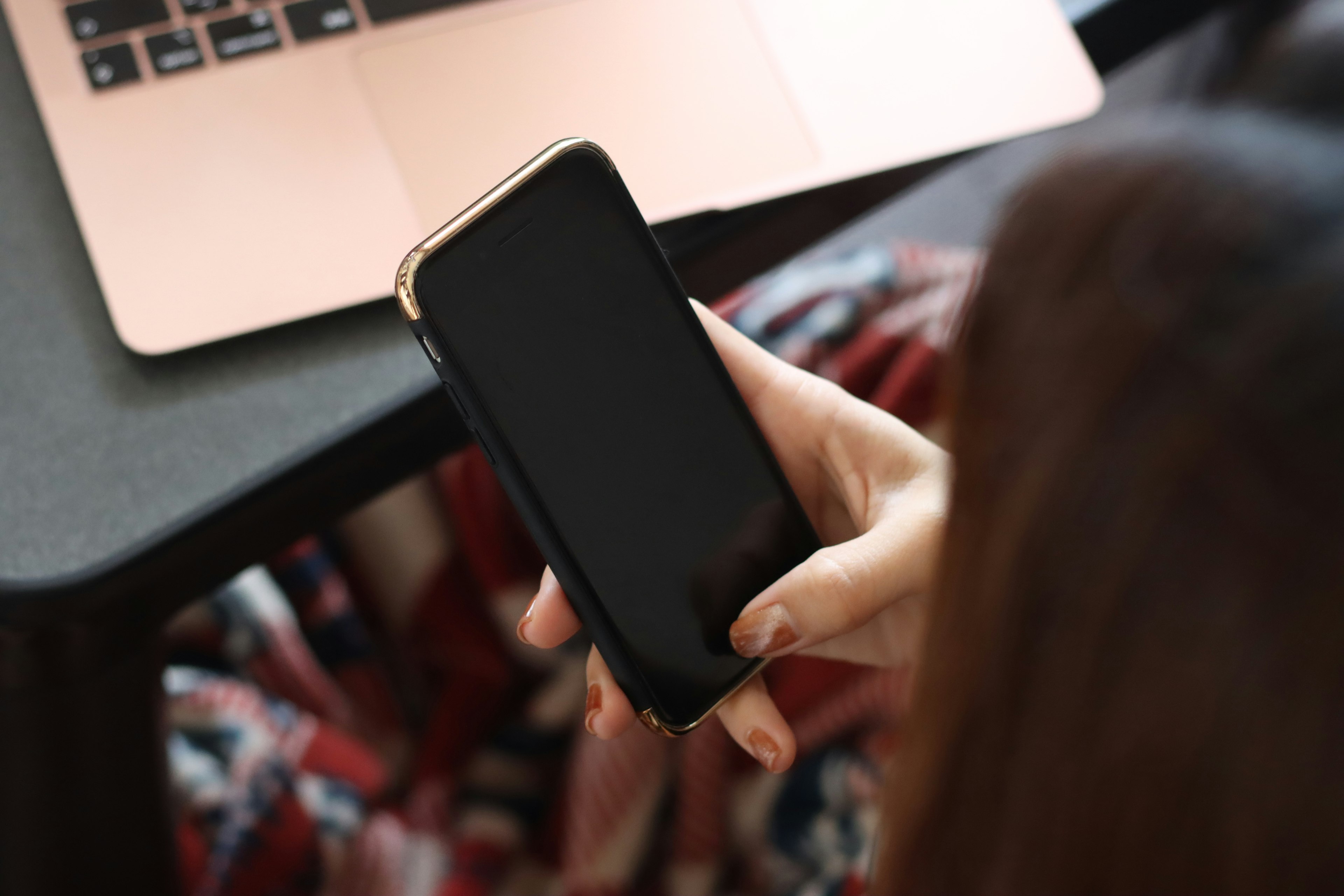 A woman holding a smartphone while working on a laptop