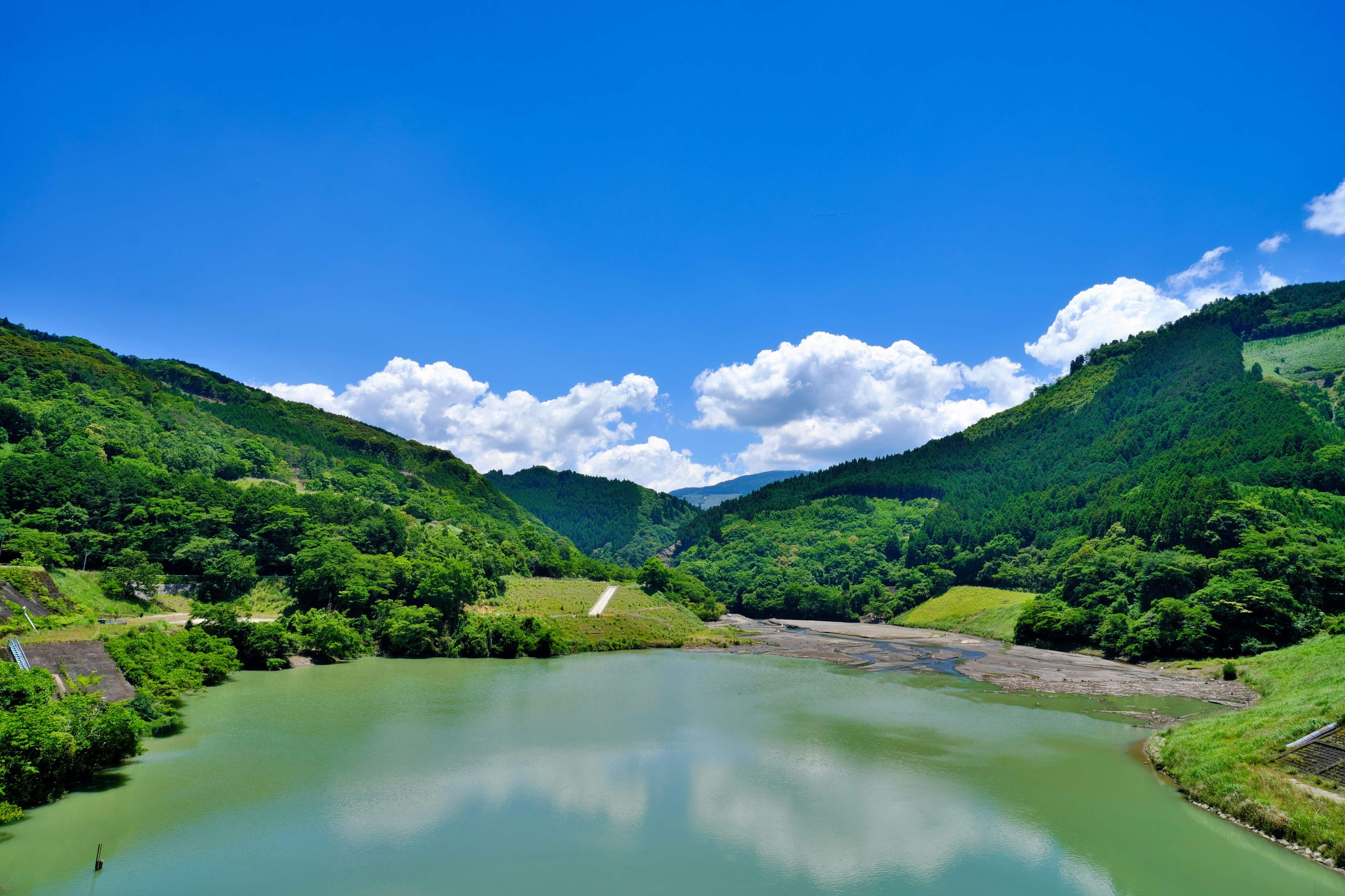 Lago sereno circondato da montagne verdi e un cielo blu chiaro