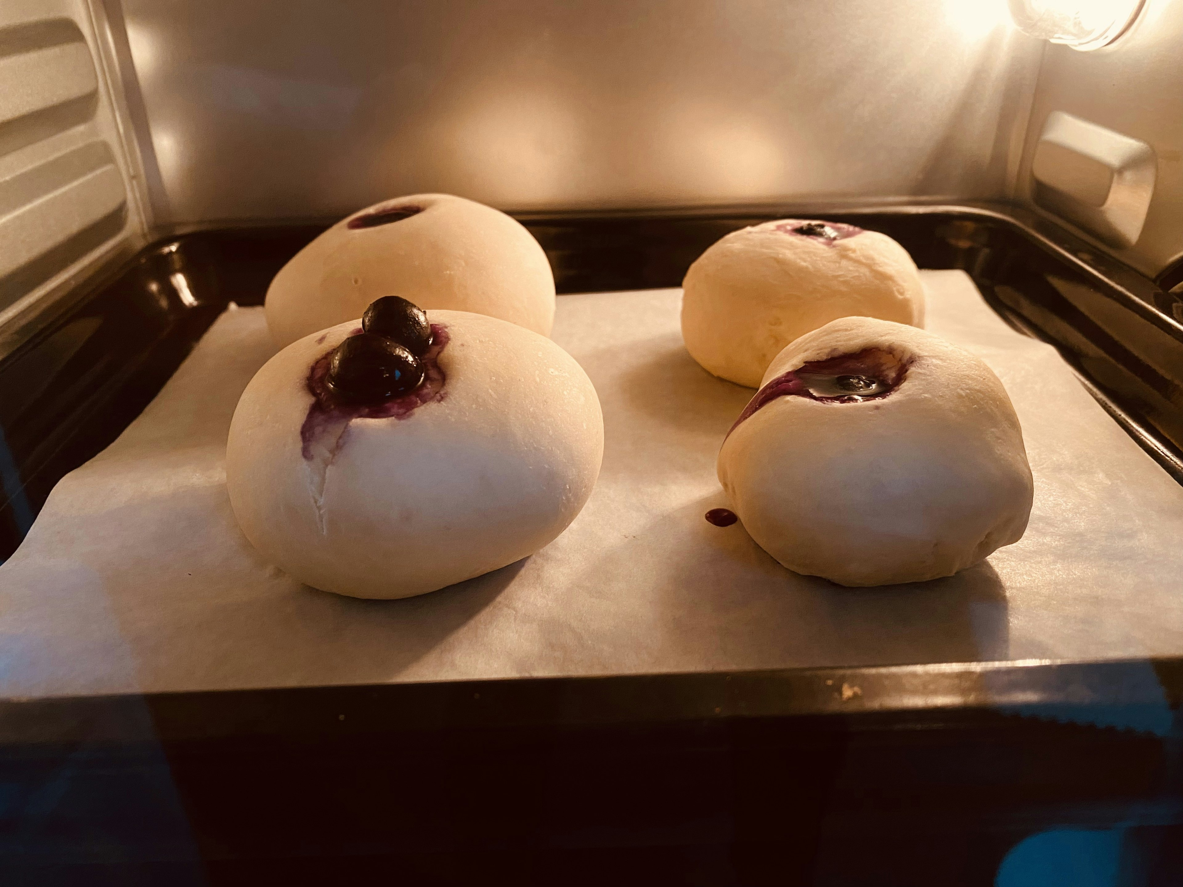 Dough buns with blueberry filling resting on a baking tray