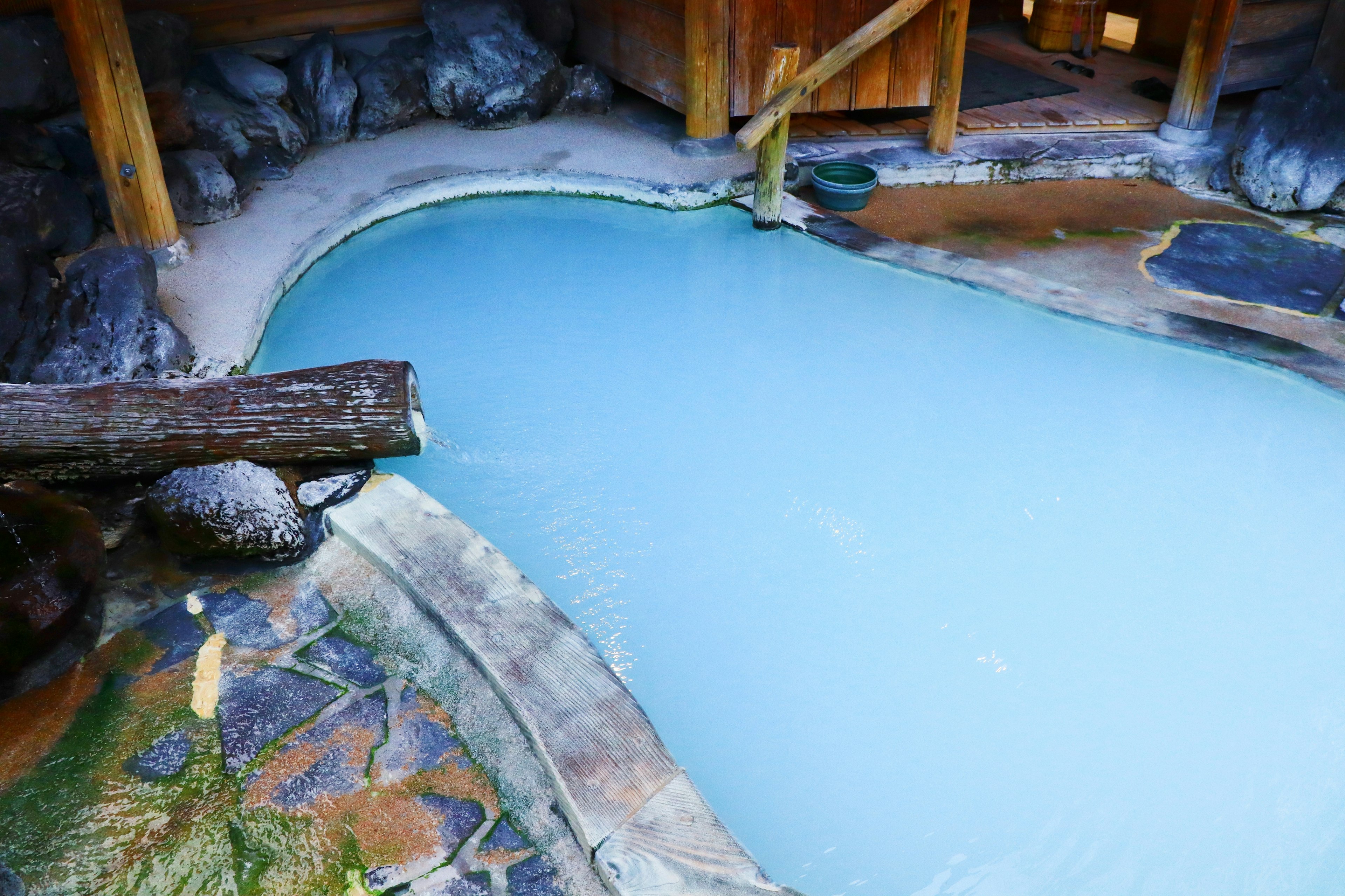 Scenic view of a blue hot spring with rocks and wooden structures