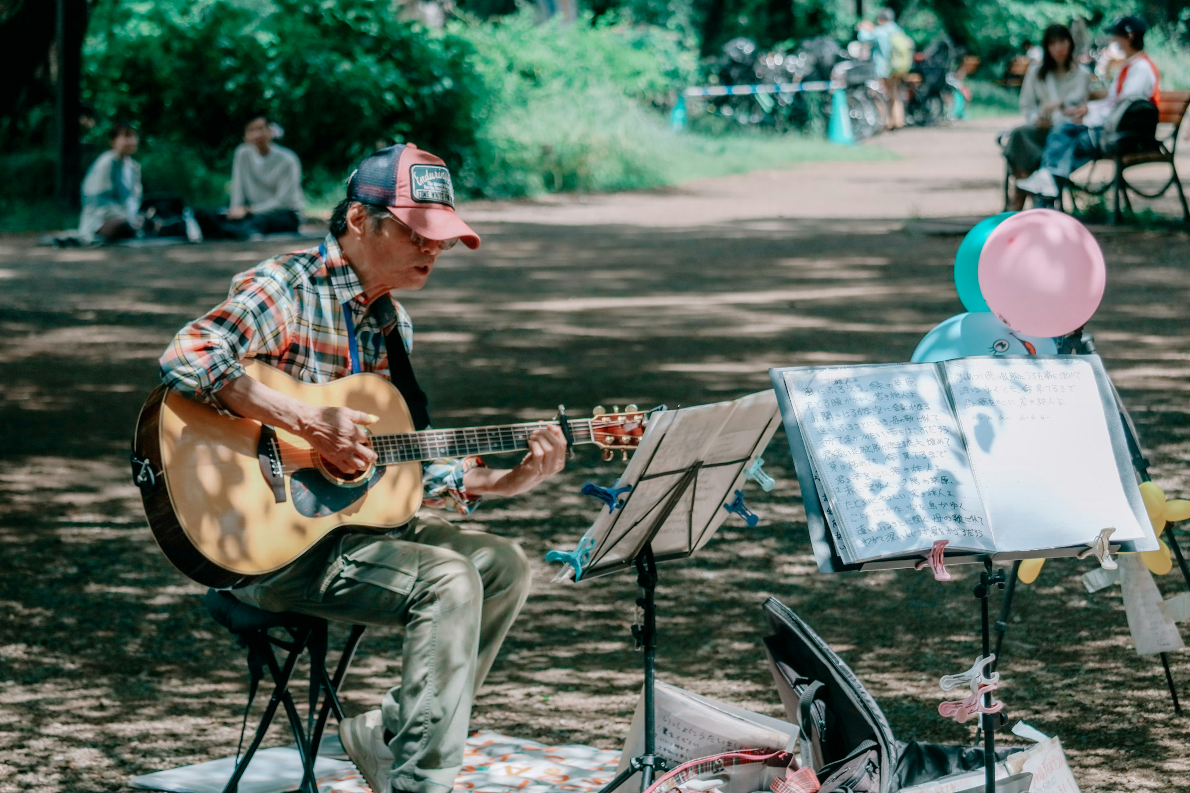 Người đàn ông chơi guitar trong công viên với những quả bóng nhiều màu sắc và bản nhạc bên cạnh