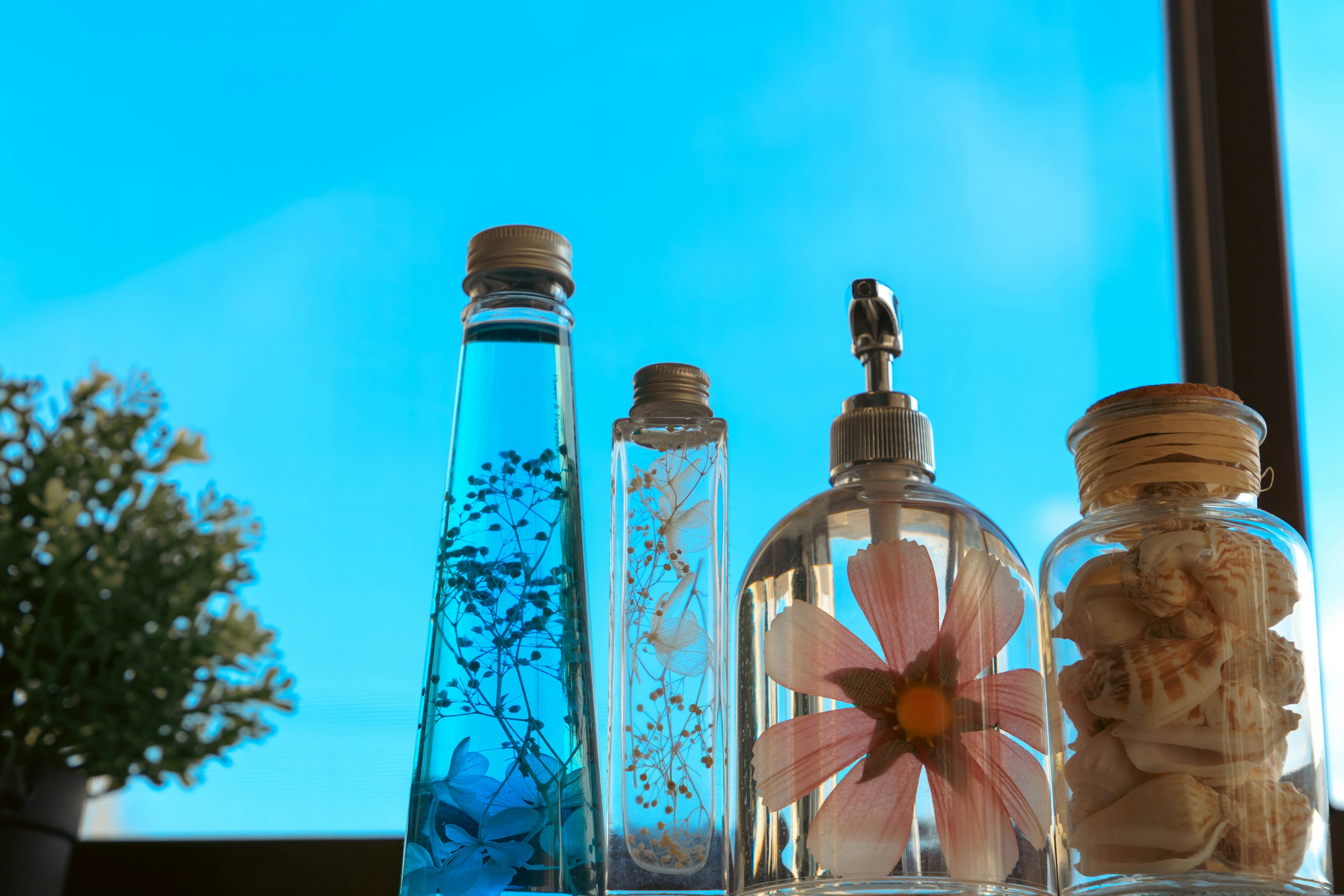 Botol transparan dengan cairan biru dan dekorasi bunga di latar belakang langit biru