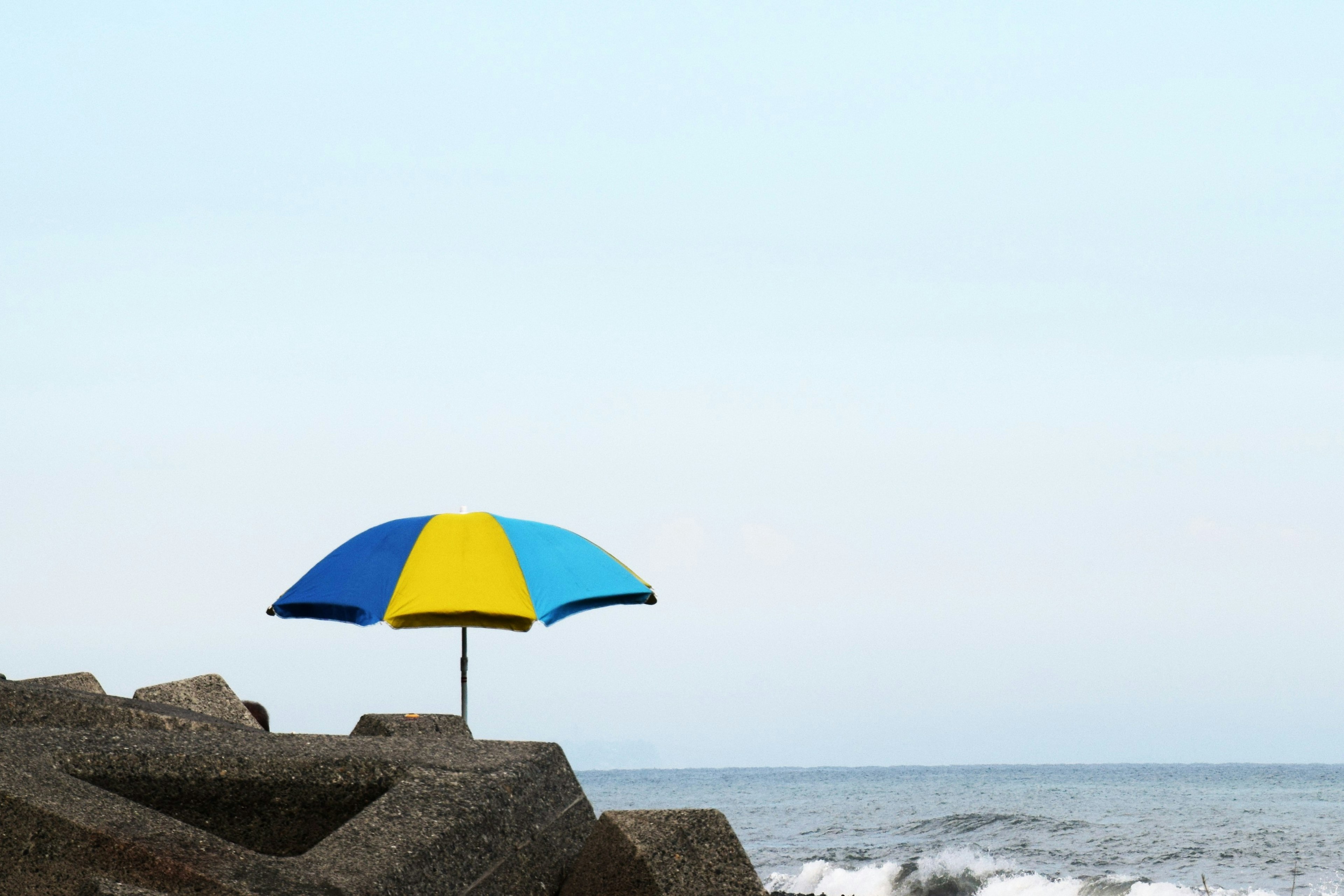 Beach umbrella in blue and yellow on rocky shore near the sea