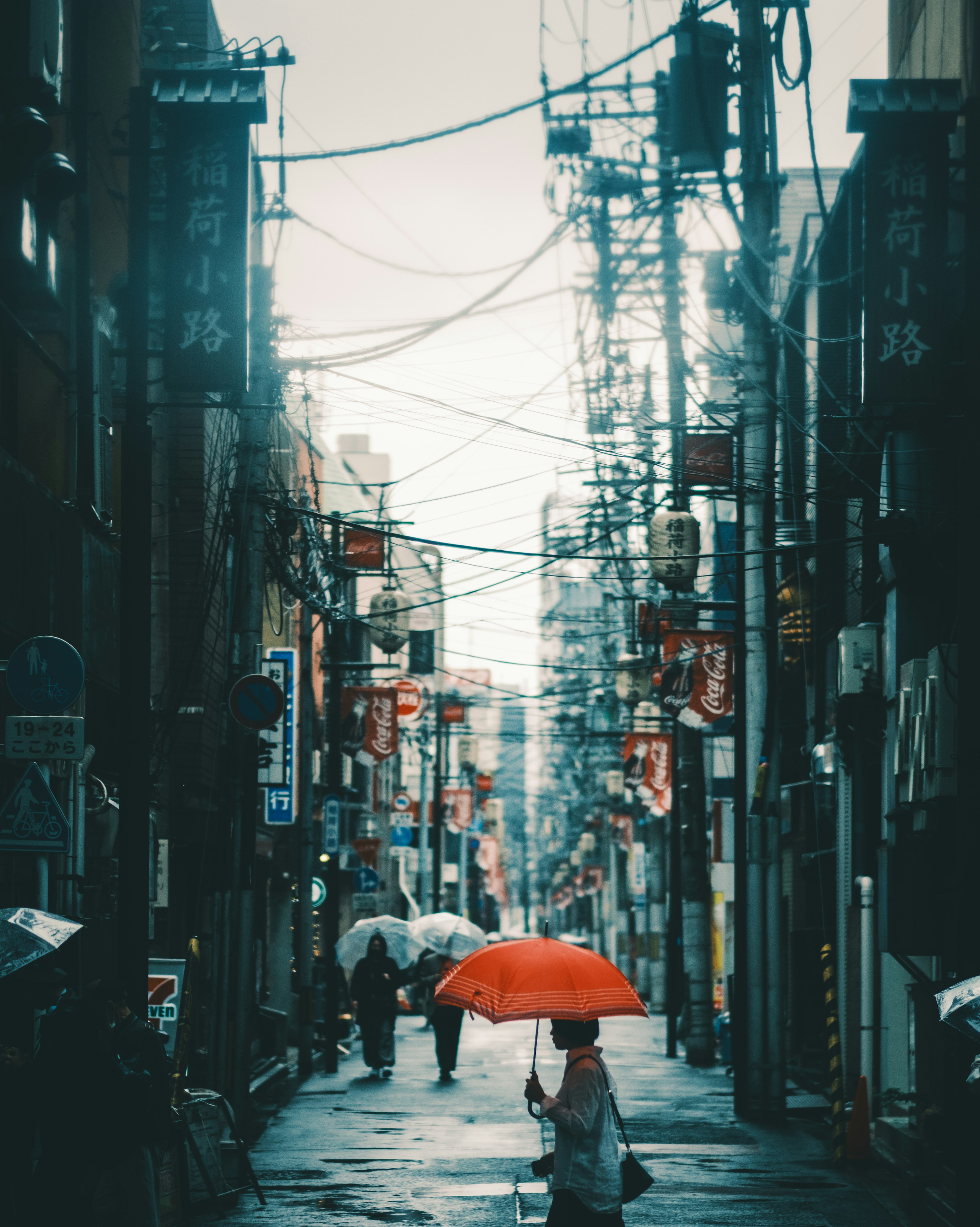 A rainy street scene with a person holding an orange umbrella and visible power lines