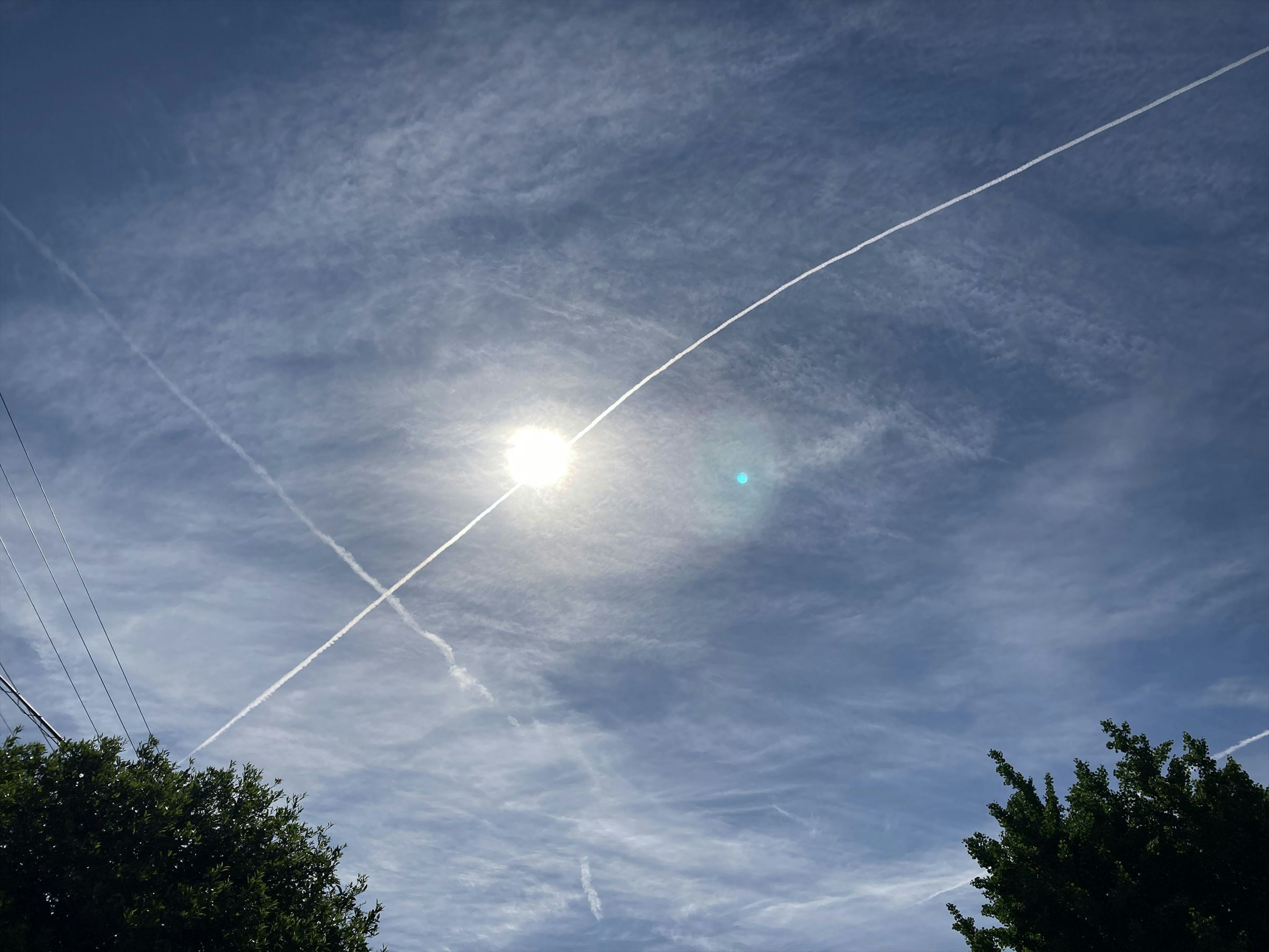 Blue sky with white contrails and a shining sun