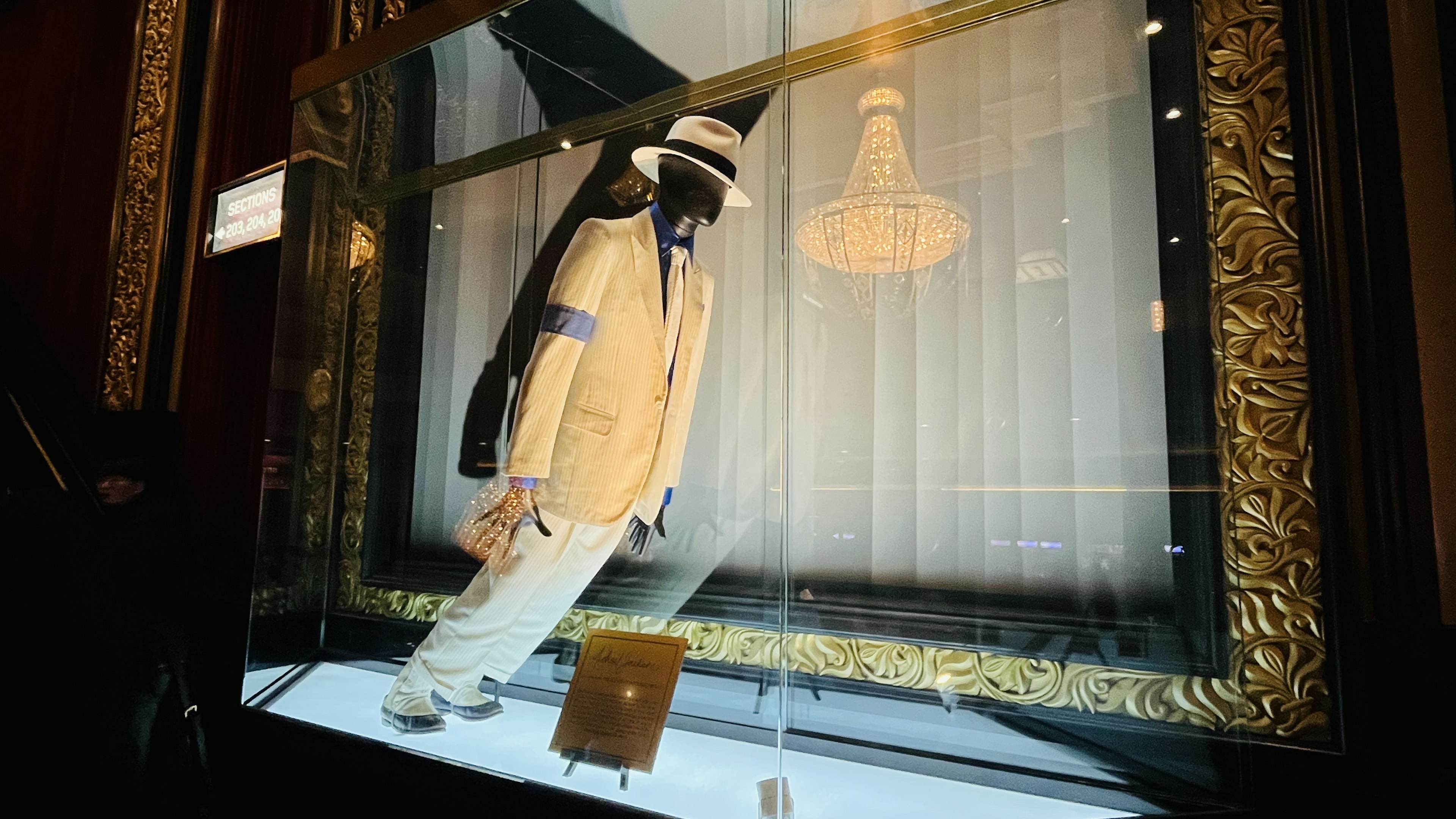 White suit and hat costume displayed in a glass case