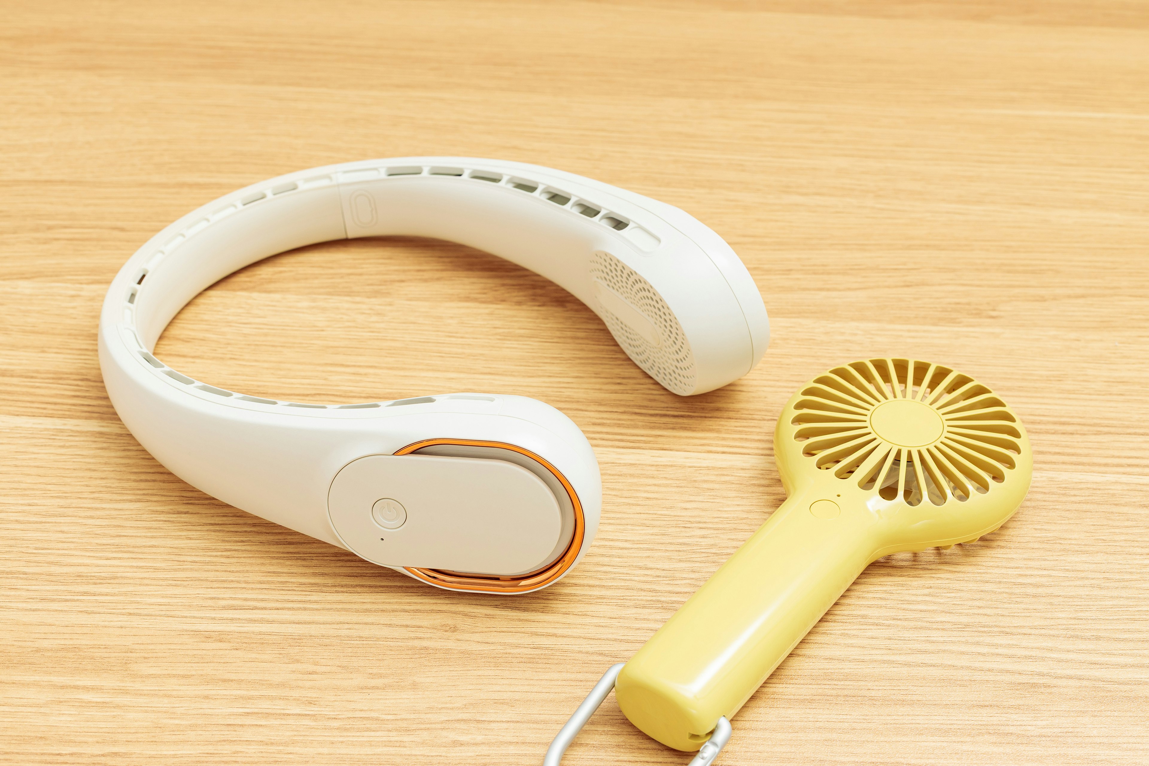 Un ventilateur de cou blanc et un ventilateur à main jaune posés sur une table en bois