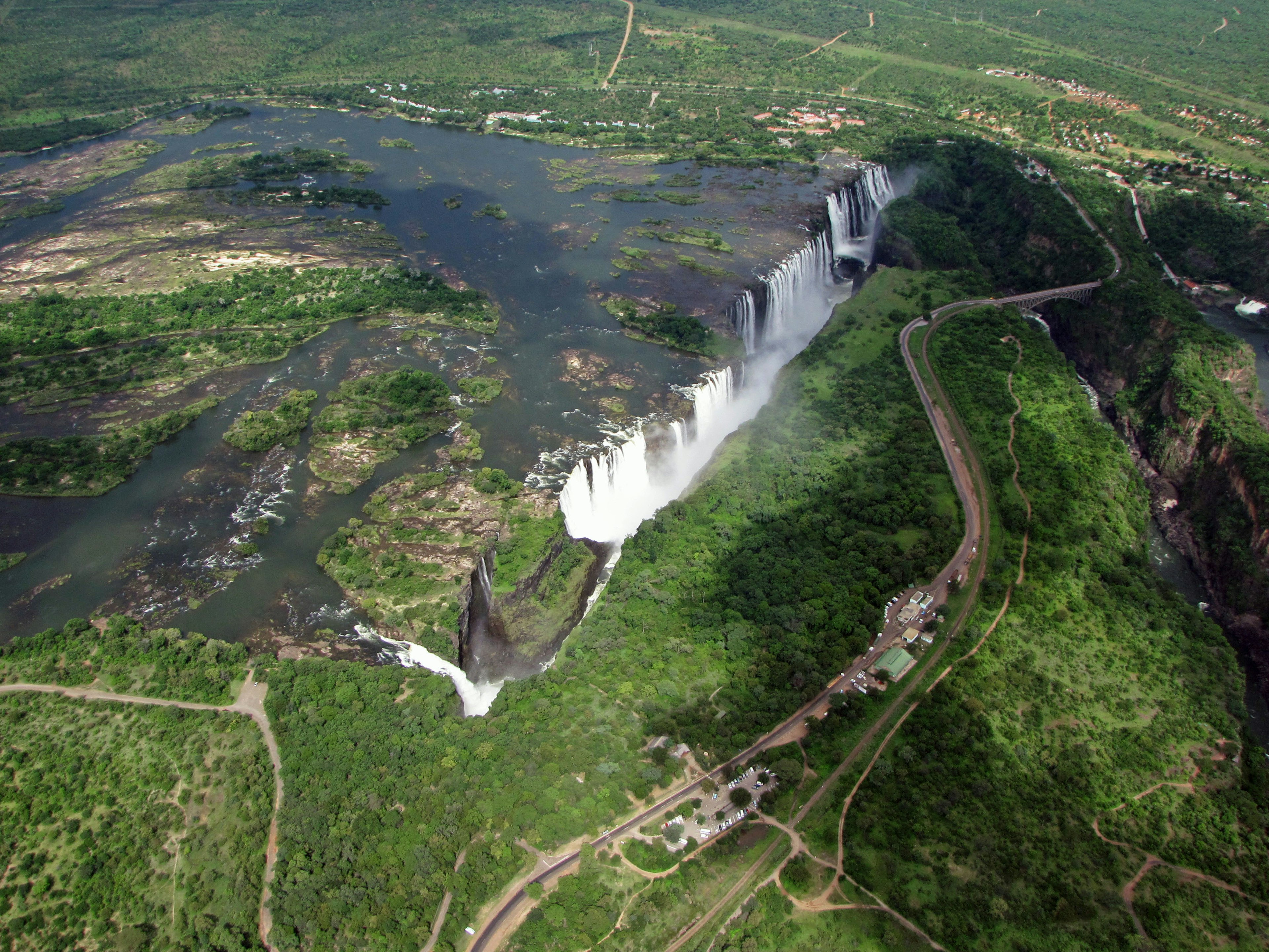 Pemandangan udara air terjun megah dikelilingi oleh pepohonan hijau subur dan aliran air