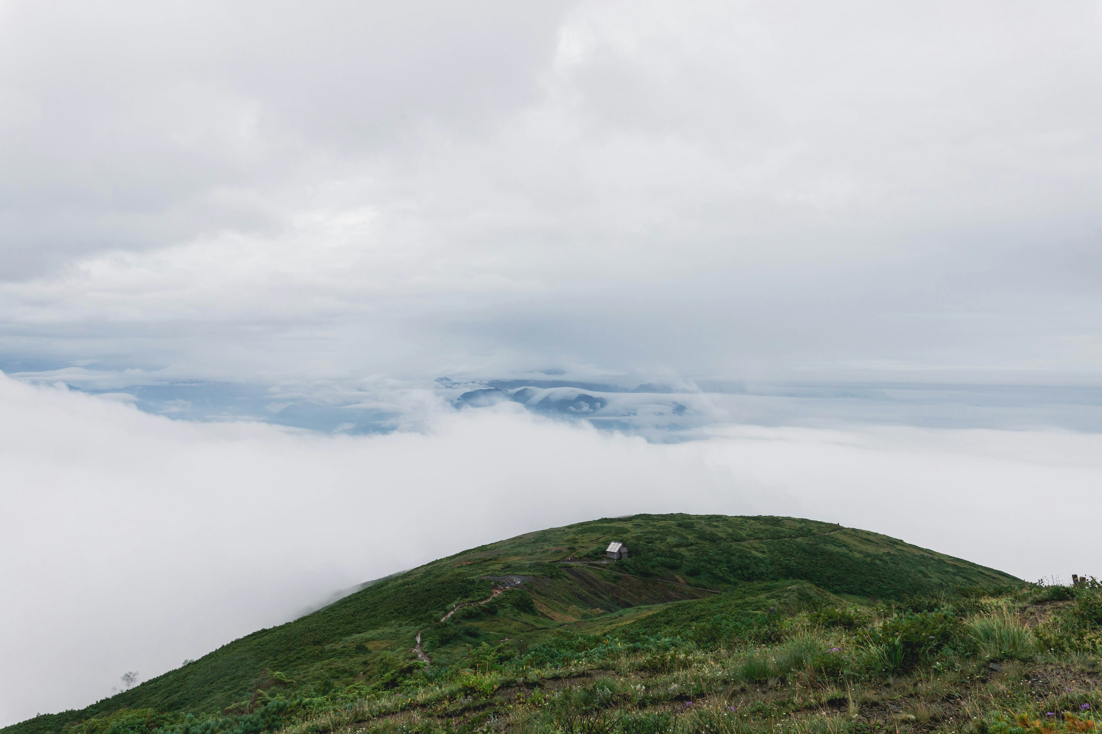 Bukit hijau di atas lautan awan dengan langit mendung