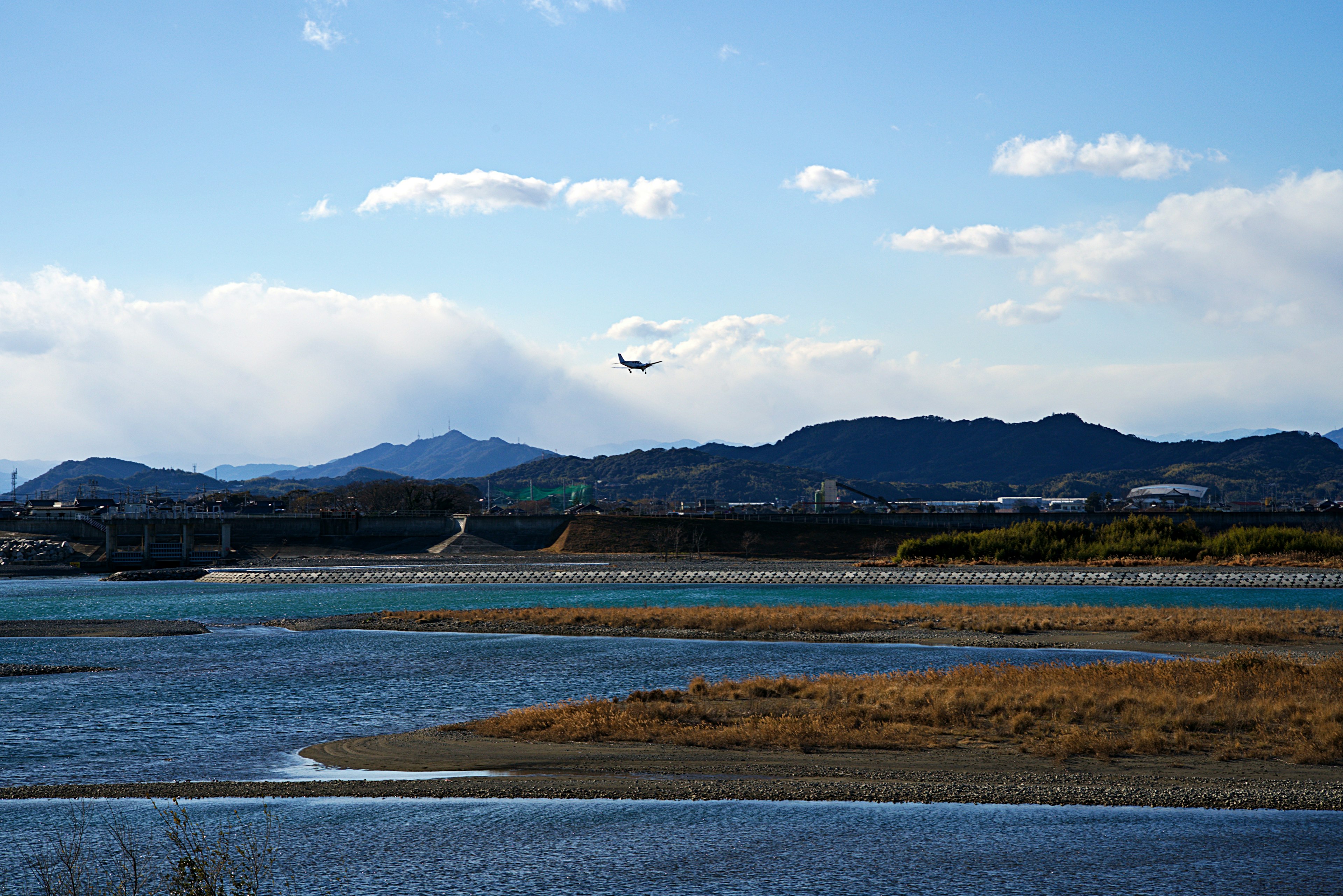 青空の下、川と山の風景にヘリコプターが飛ぶ