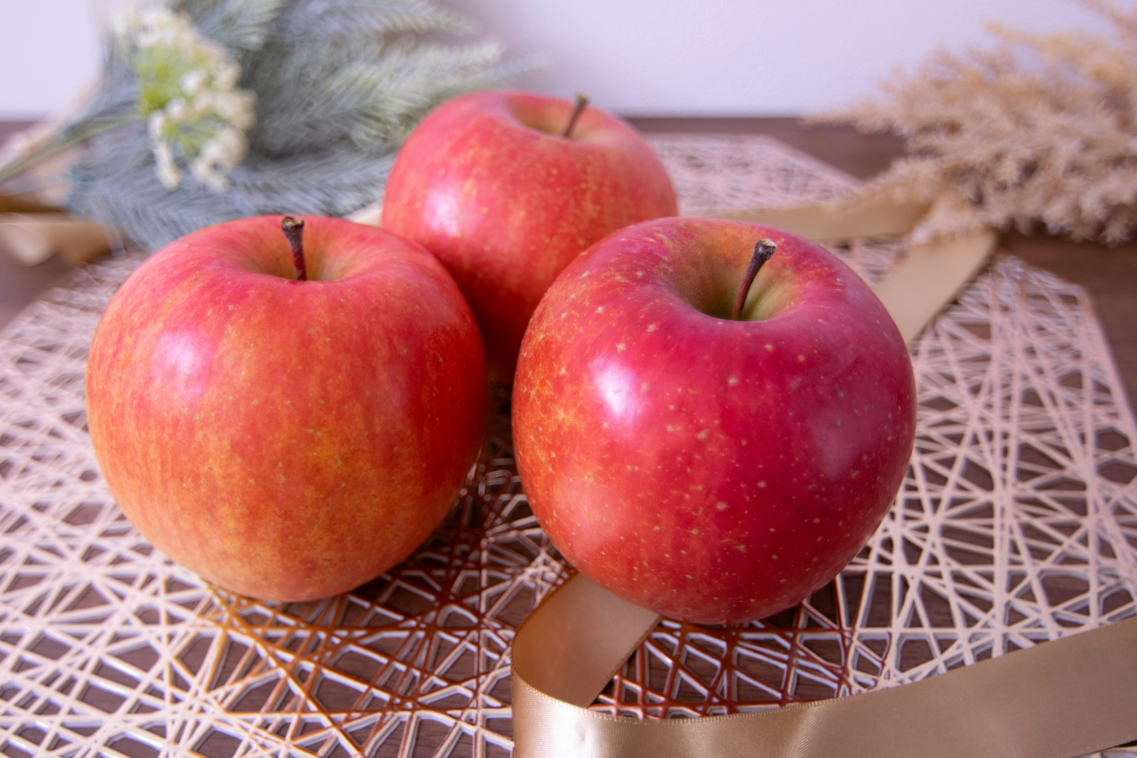 Tres manzanas rojas sobre un tapete decorativo con flores secas al fondo