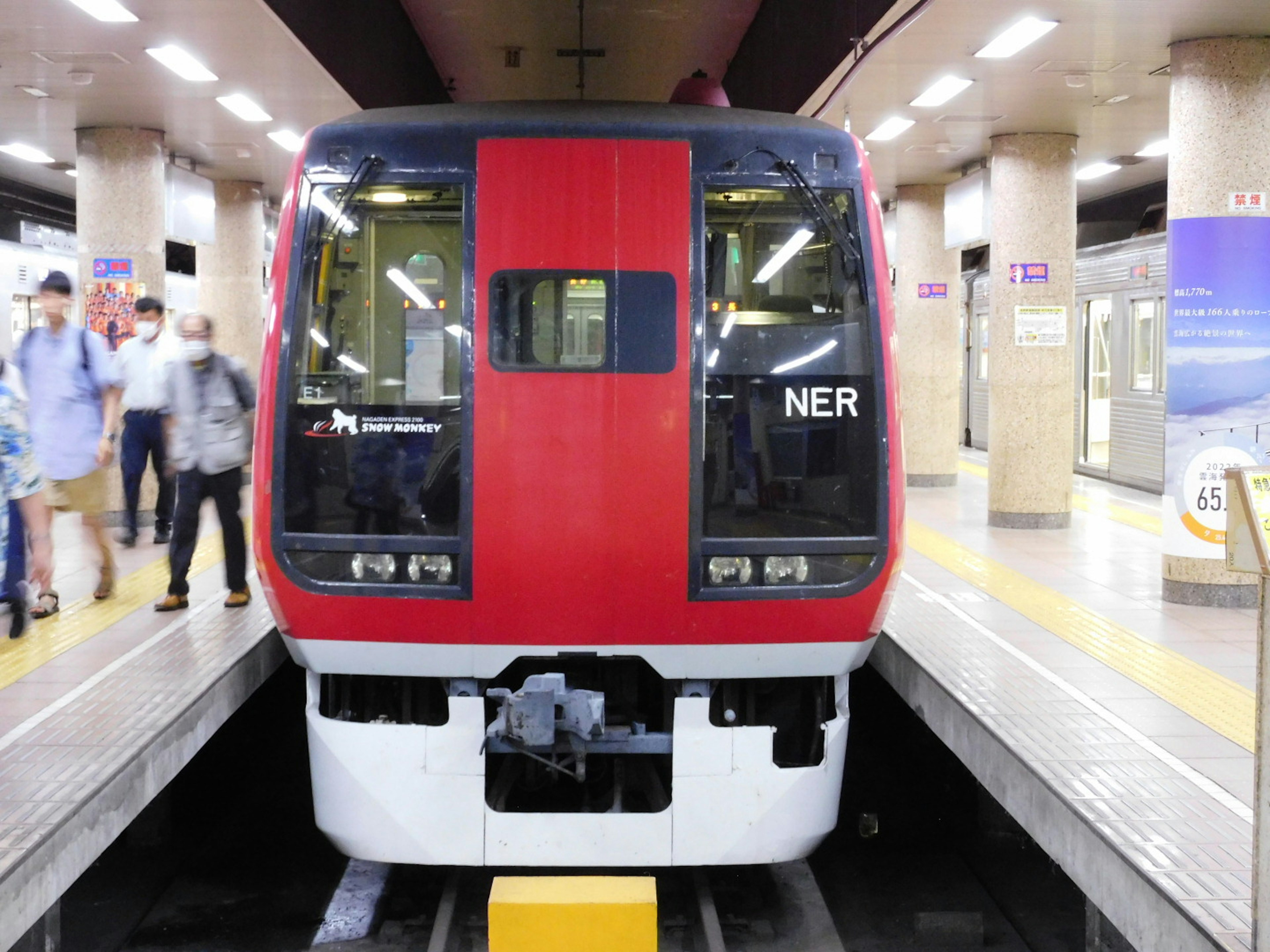 赤い電車が駅に停車している状況 周囲には乗客がいる