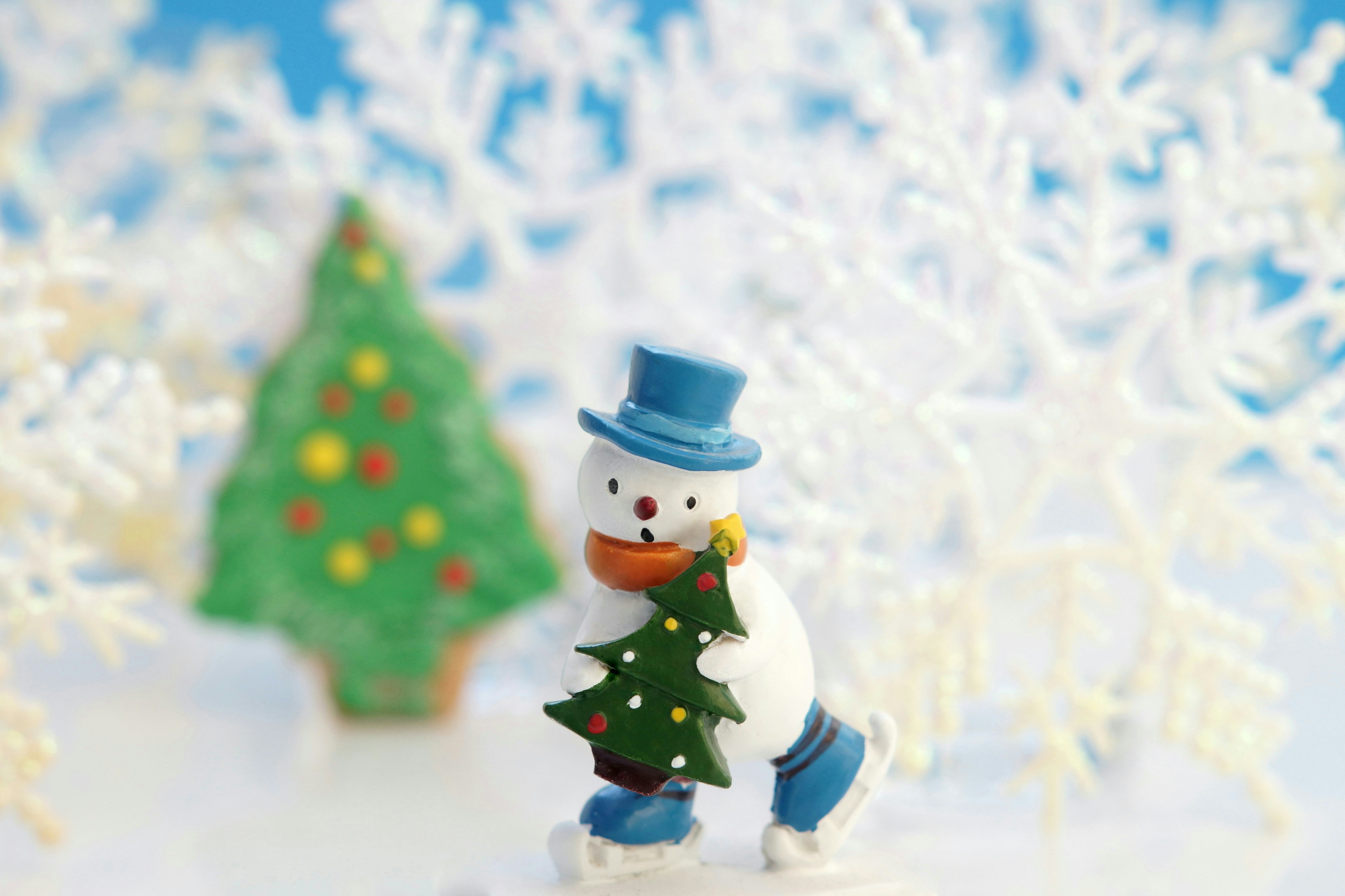 Un bonhomme de neige tenant un petit sapin de Noël avec des flocons de neige en arrière-plan