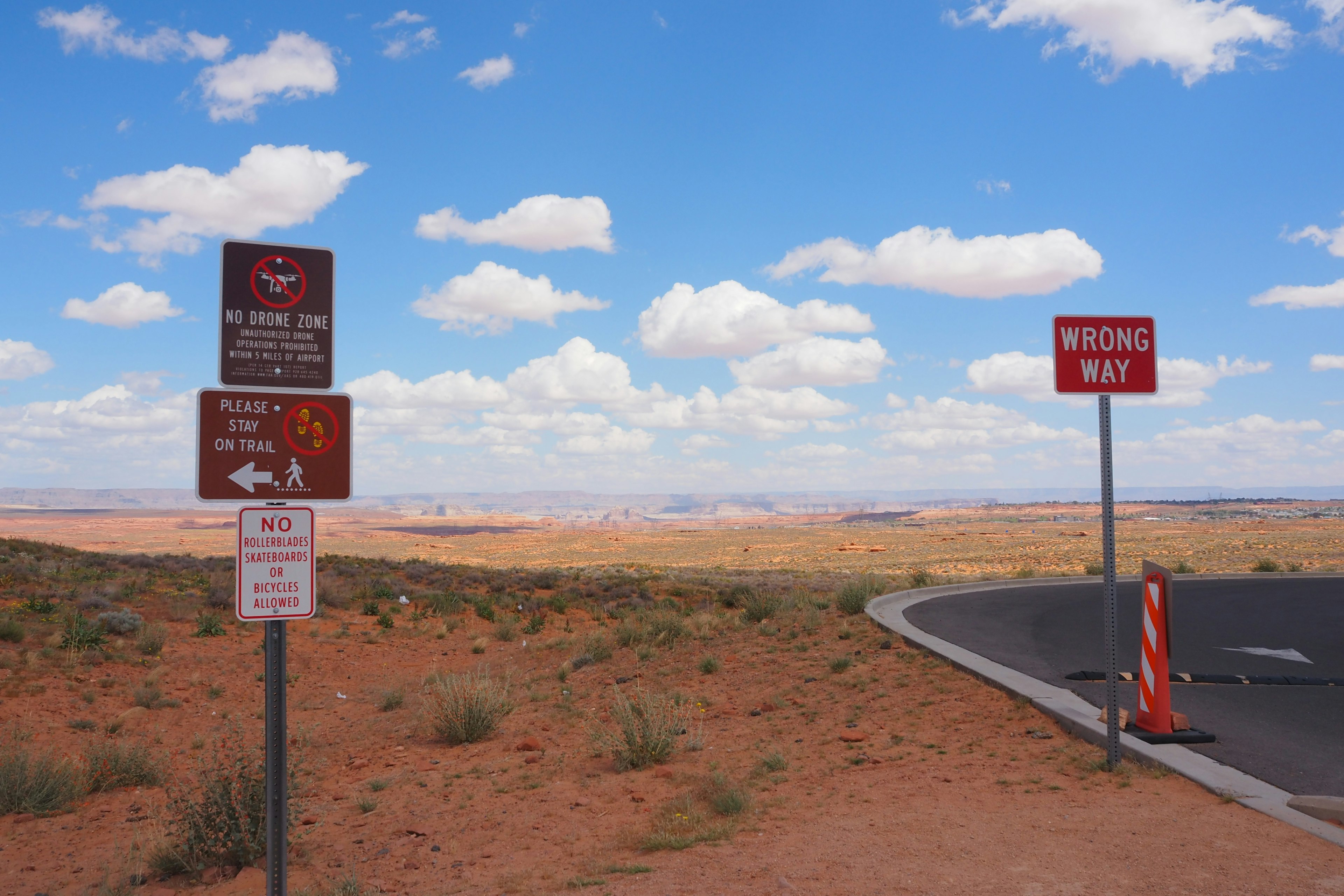 Eine Ansammlung von Verkehrsschildern vor einer weiten Wüstenlandschaft und blauem Himmel