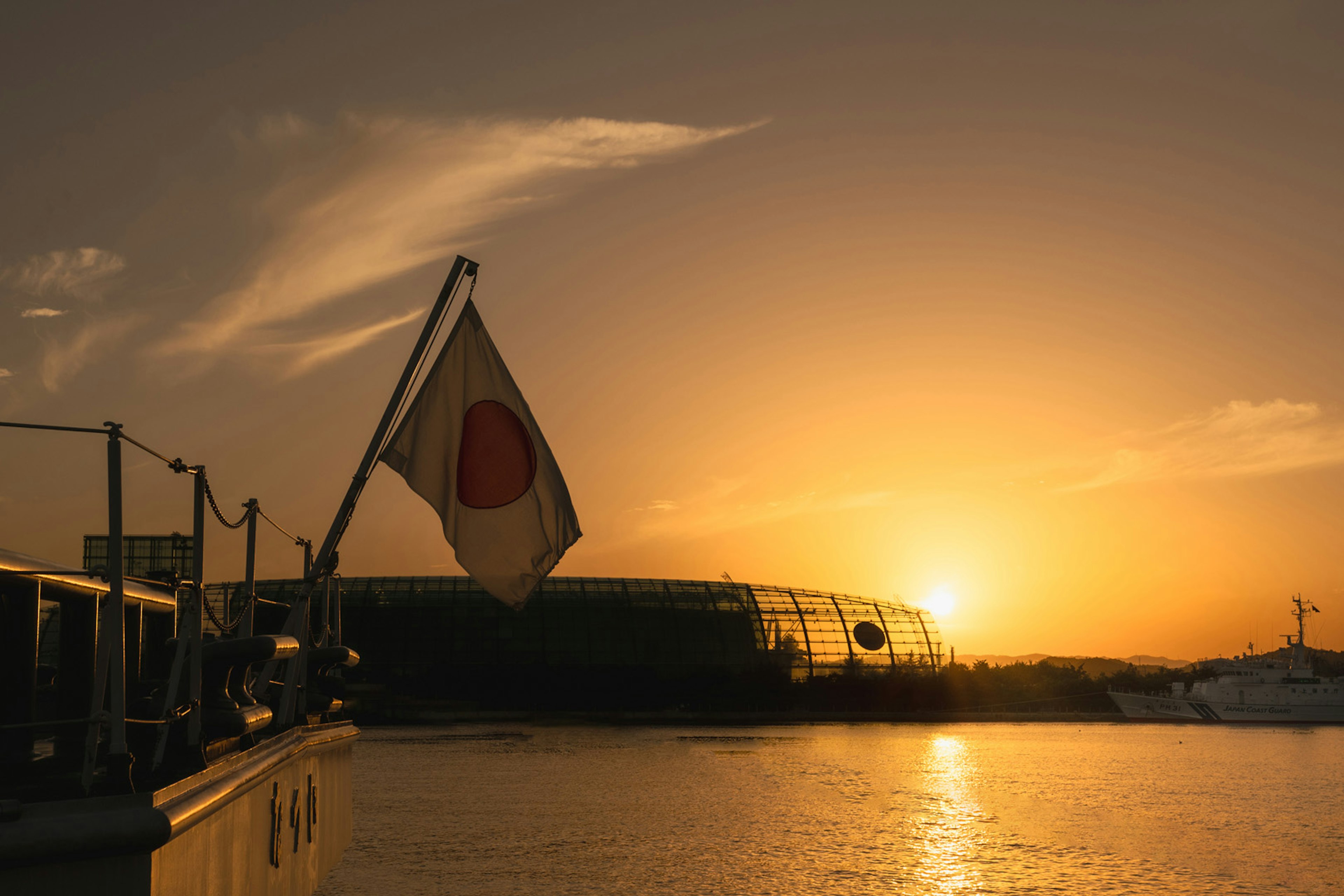 Japanische Flagge weht gegen einen Sonnenuntergang über Wasser