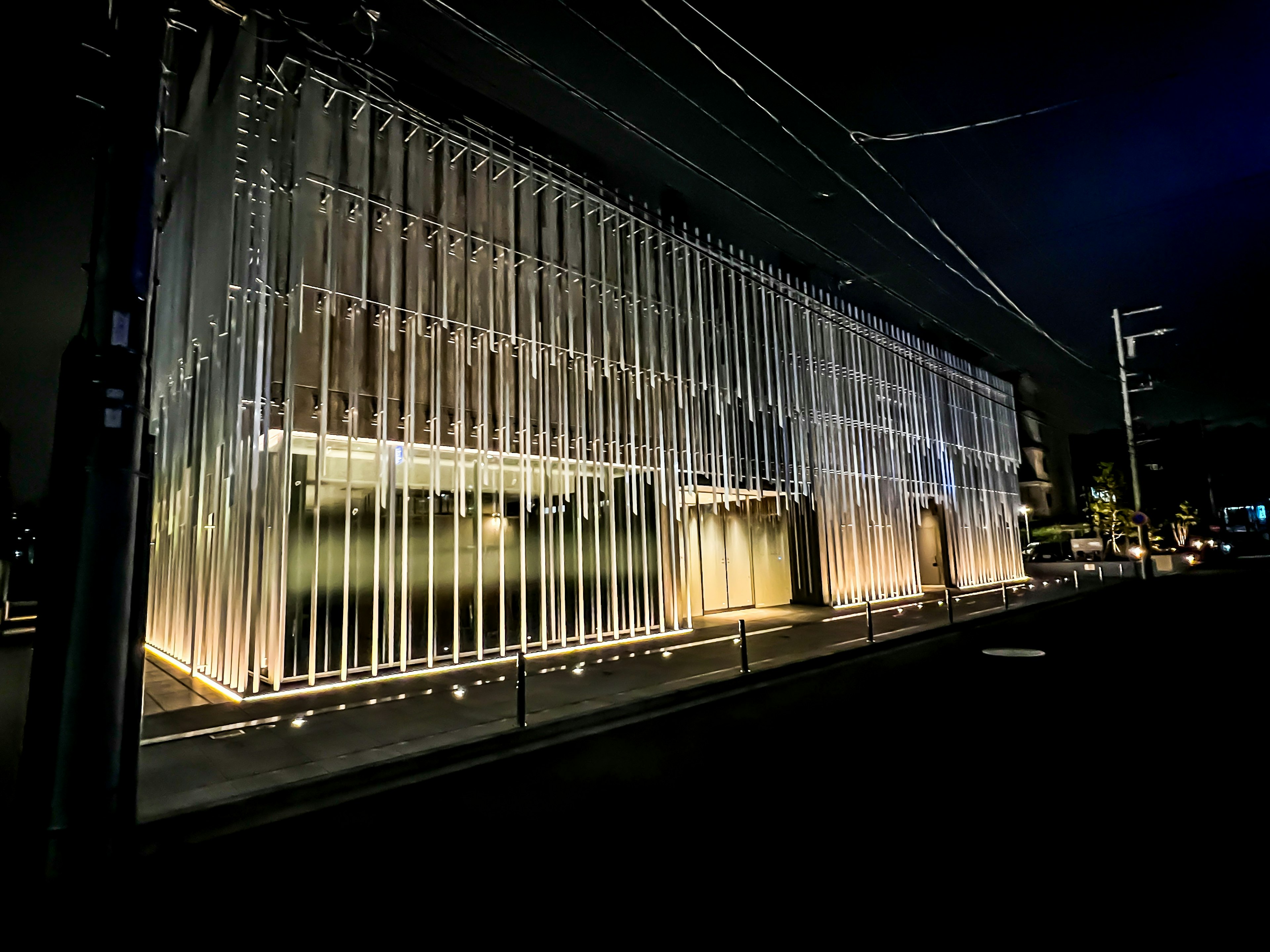 Modern glass building illuminated at night featuring bright lighting and striped design