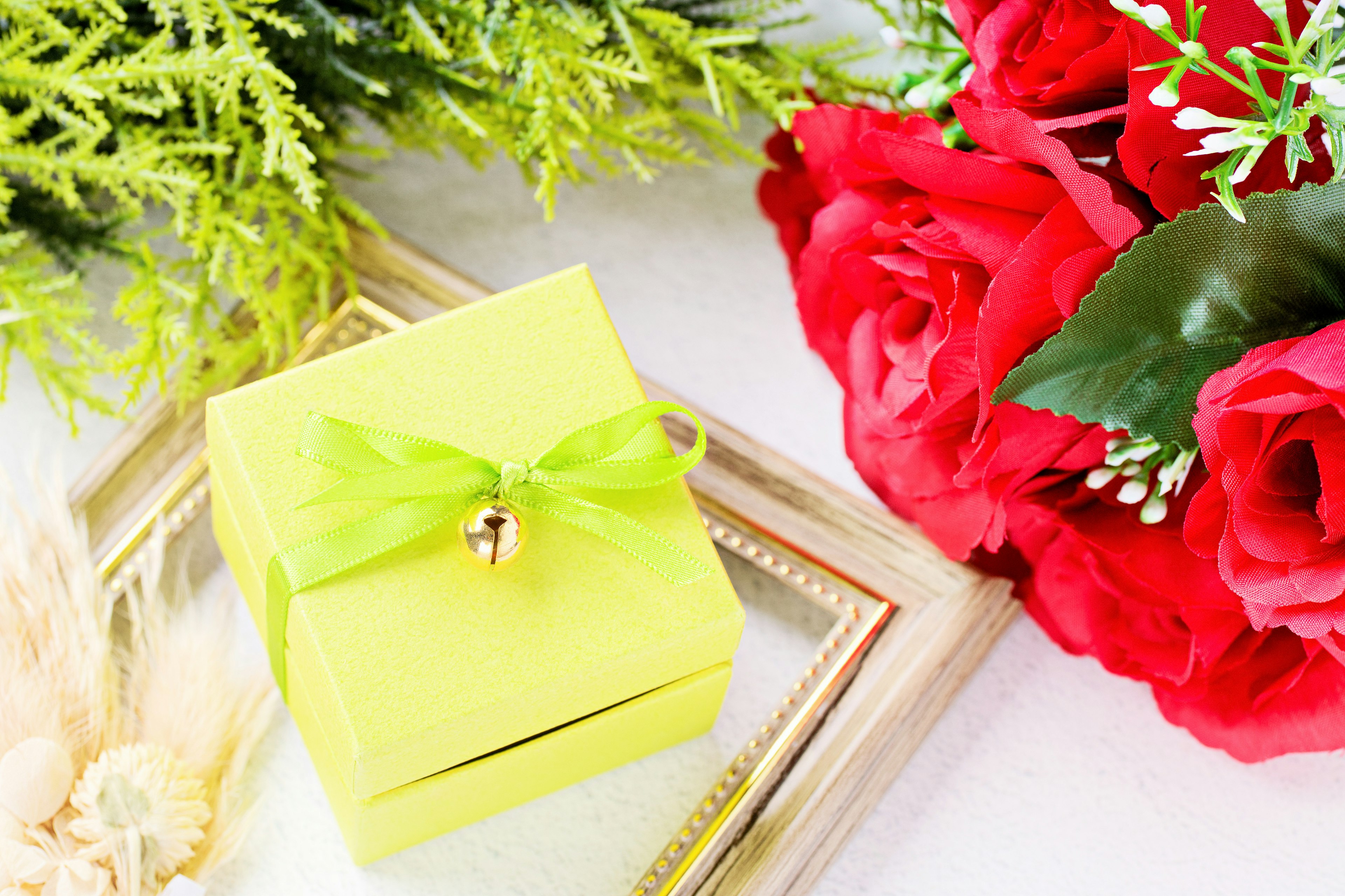 A yellow gift box with a green ribbon beside red roses