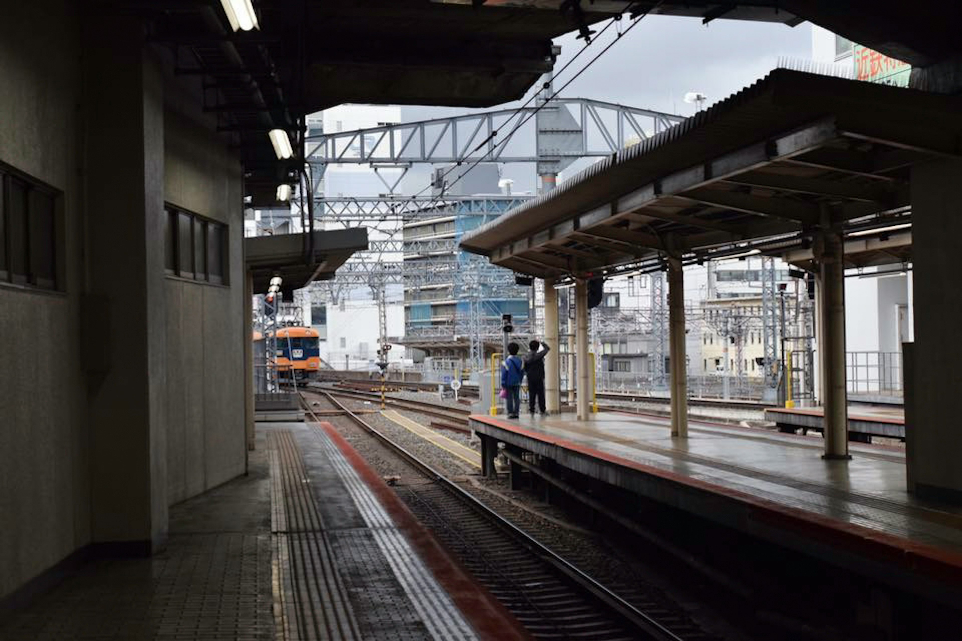 駅のプラットフォームに立つ二人の作業員と周囲の工事現場