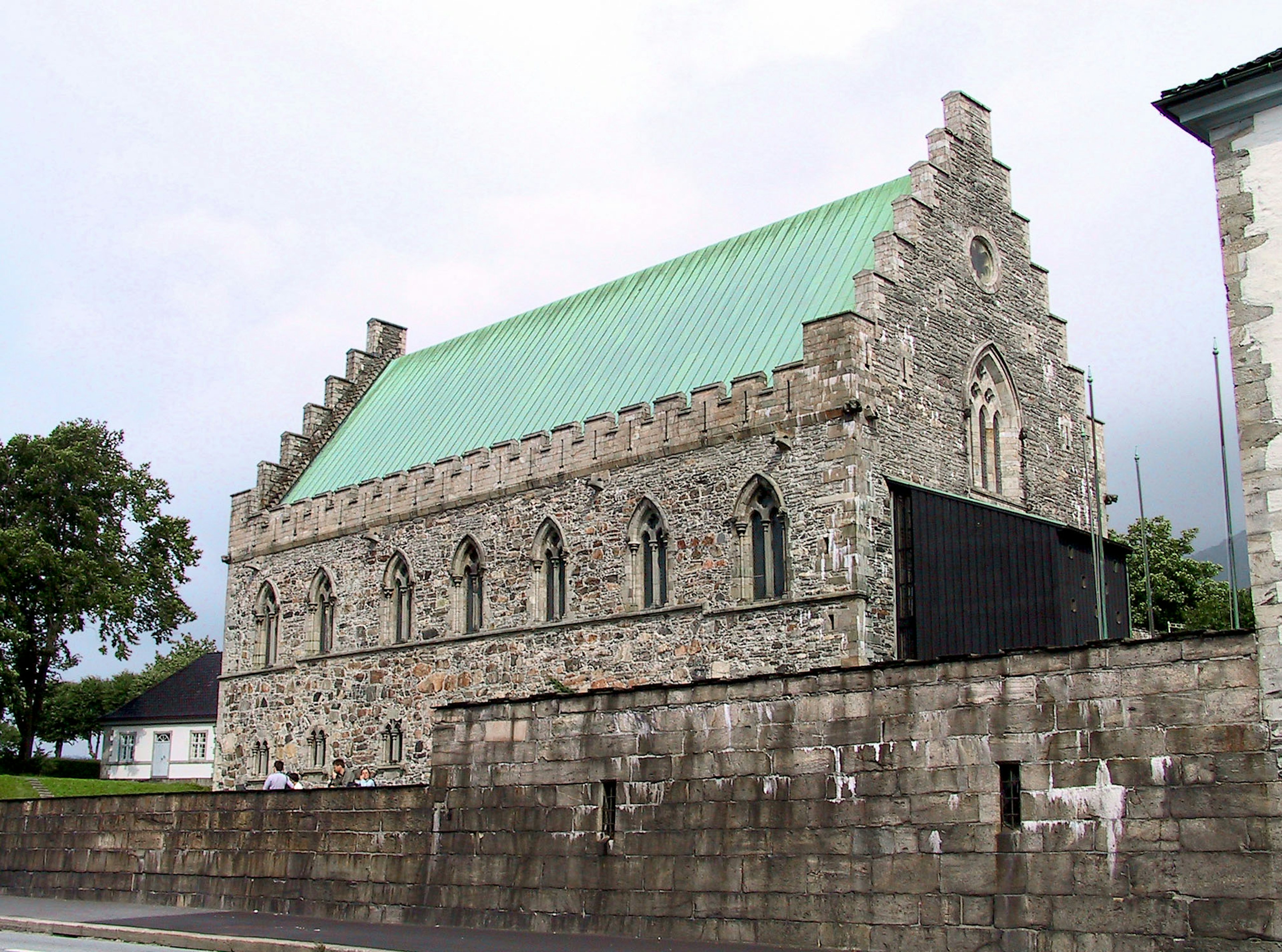 Exterior de una iglesia de piedra con un techo verde y frontones distintivos rodeada de paisaje